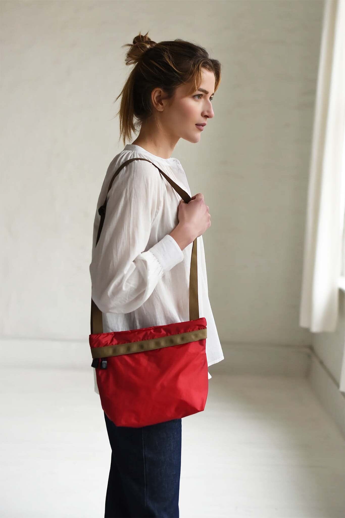 Woman holding a red bag with a strap over her shoulder in a minimalistic setting.