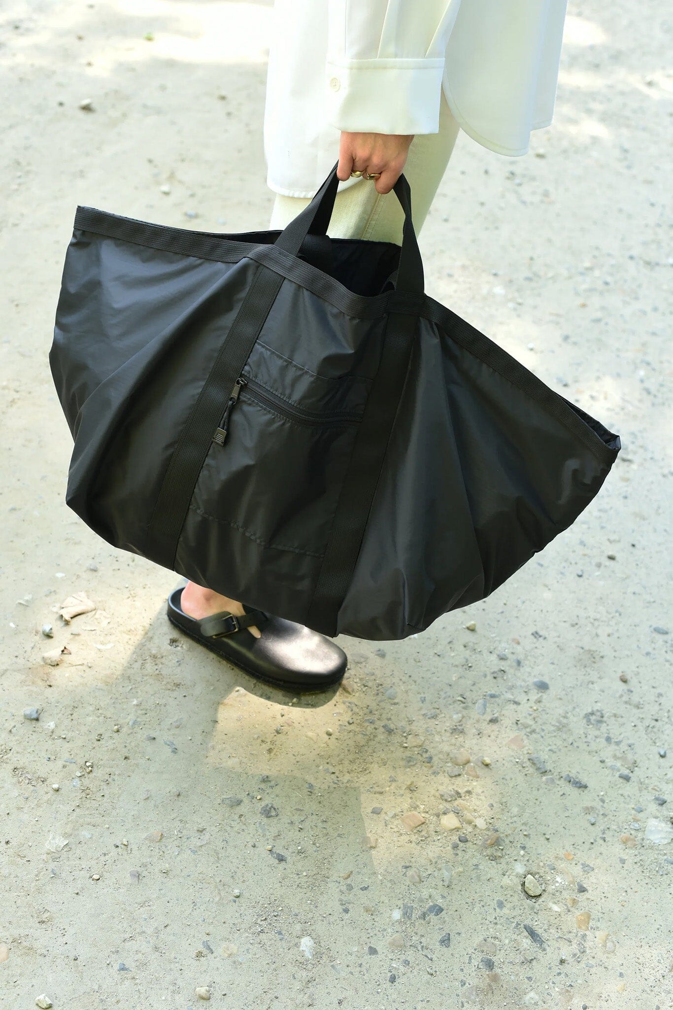 Person holding a large black zipper bag on a concrete surface