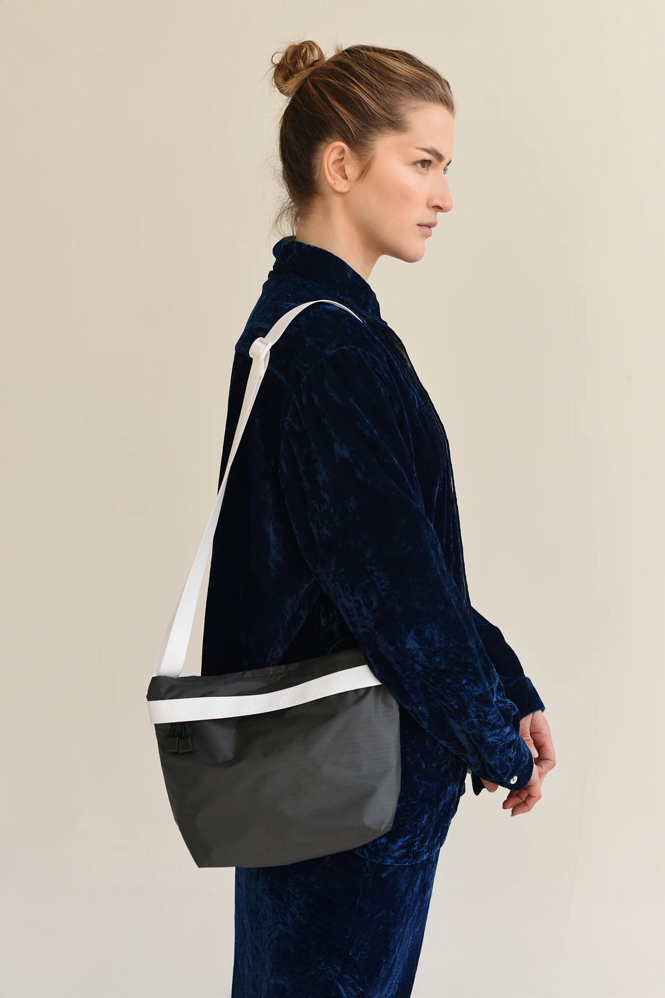 Woman wearing a dark blue jacket with a black and white crossbody bag on a beige background