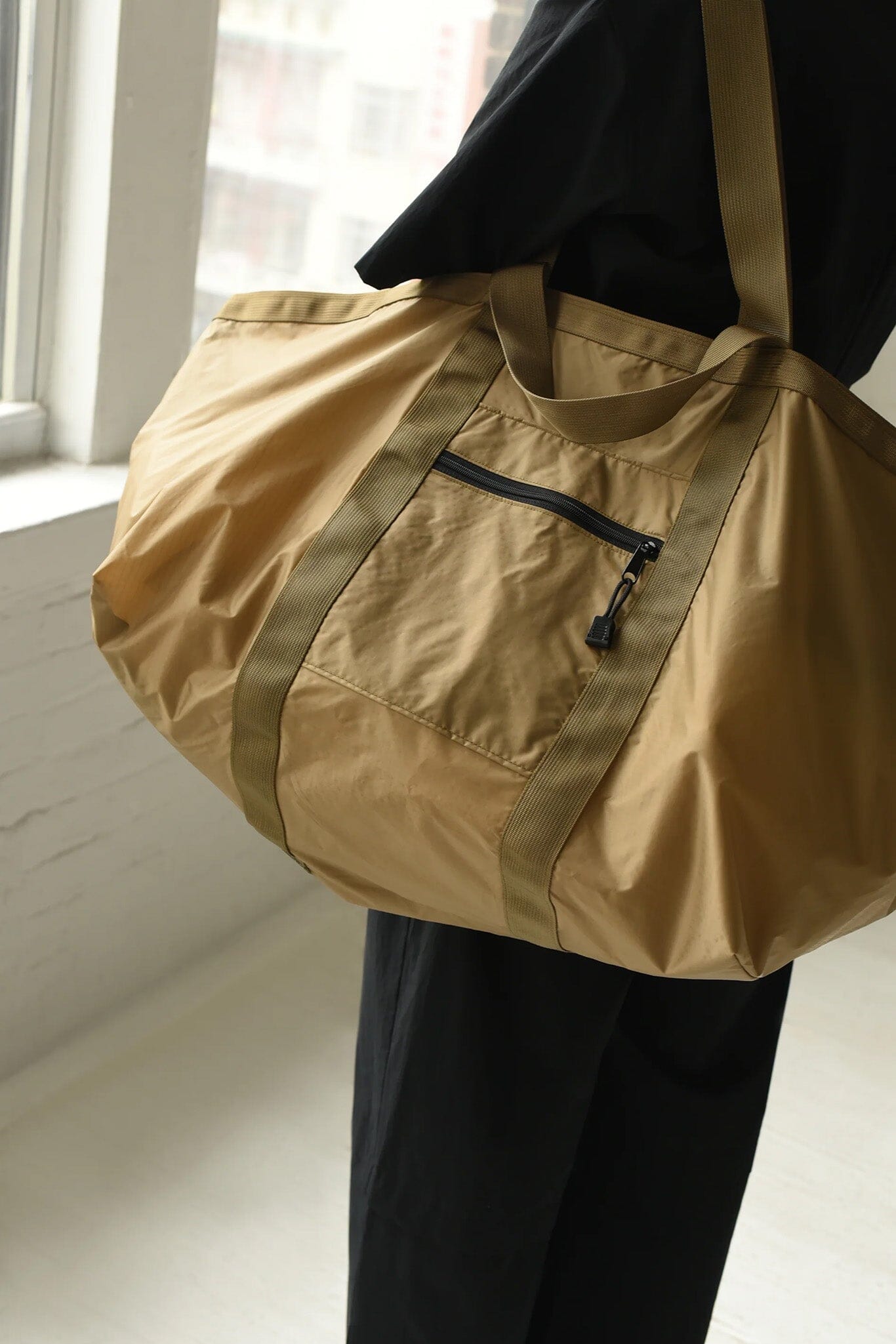 Person holding a light brown duffel bag with a strap over shoulder.