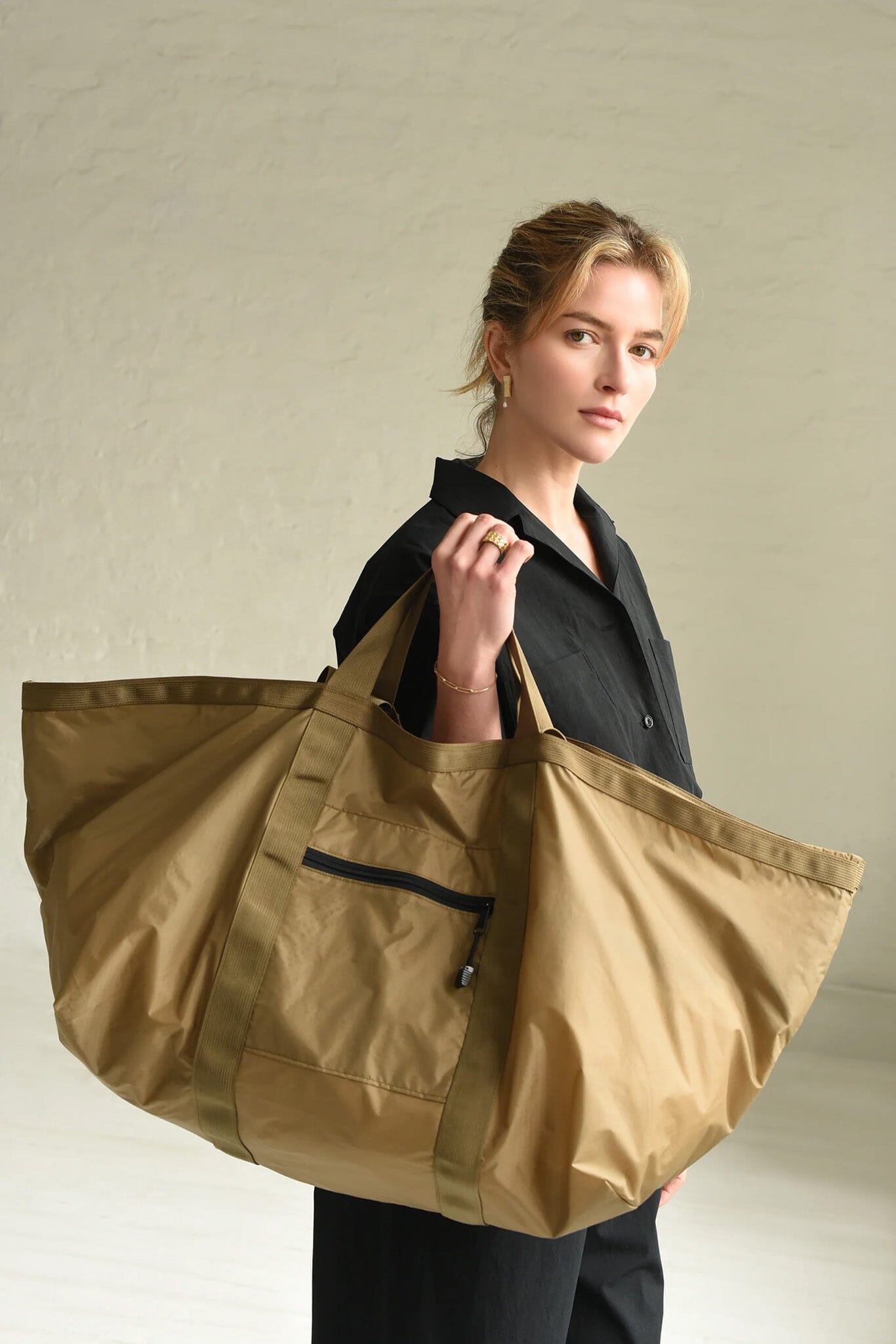 Woman holding a large brown tote bag against a neutral background