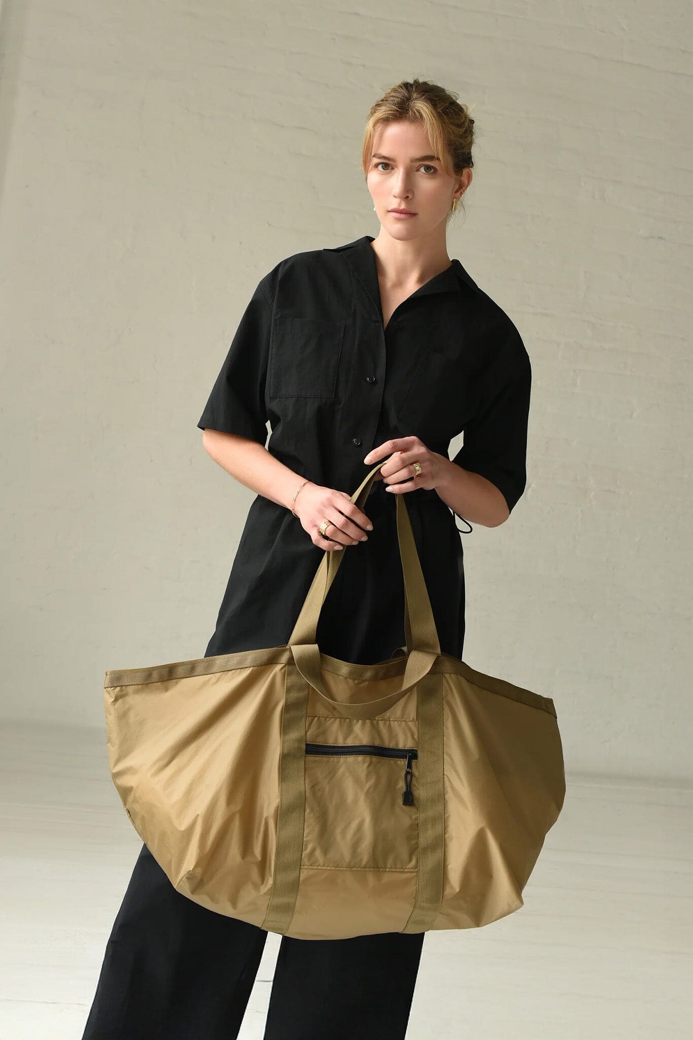 Woman holding a brown and green large tote bag against a plain background