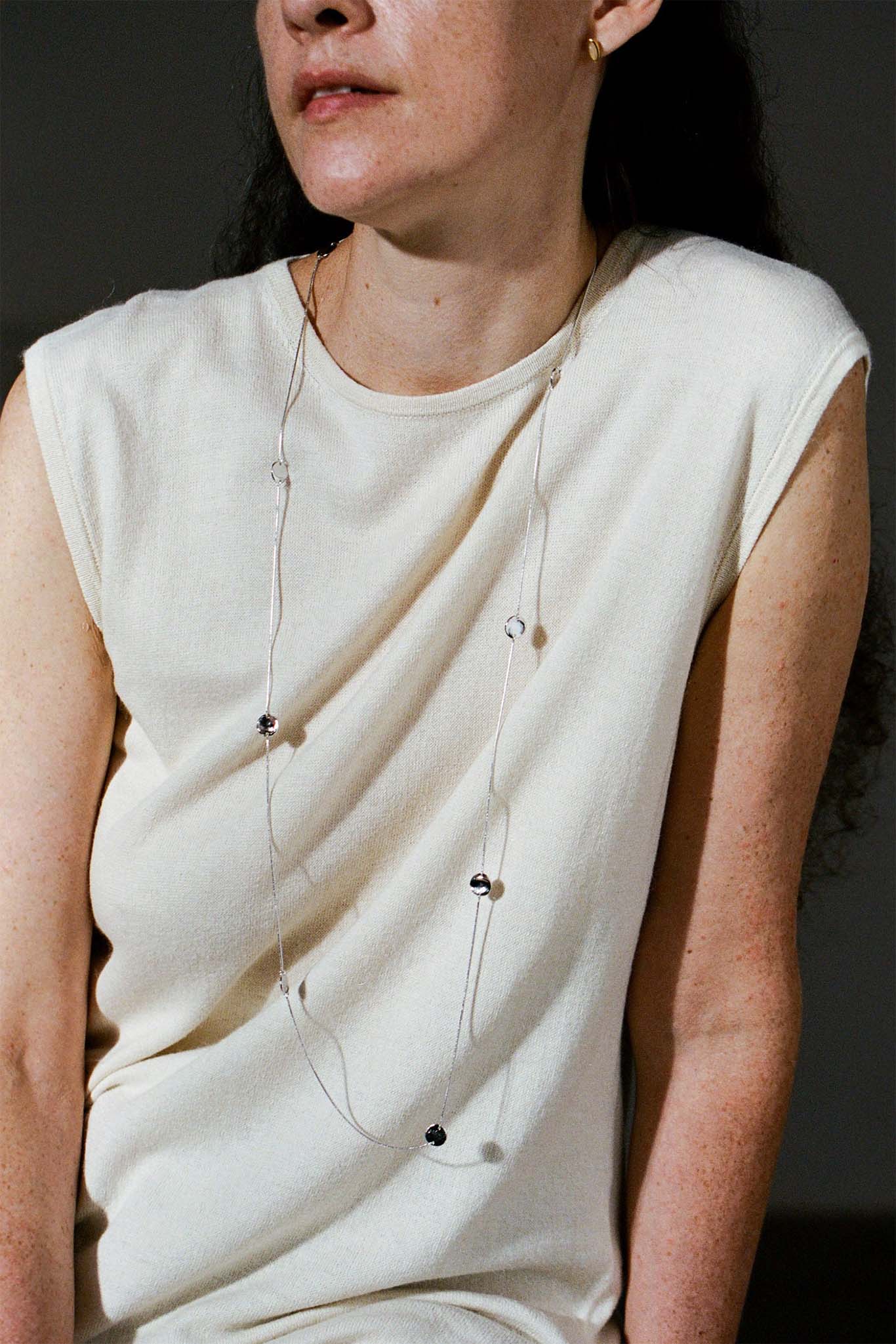 Woman wearing a cream sleeveless top with long sterling silver circle necklace against a dark background