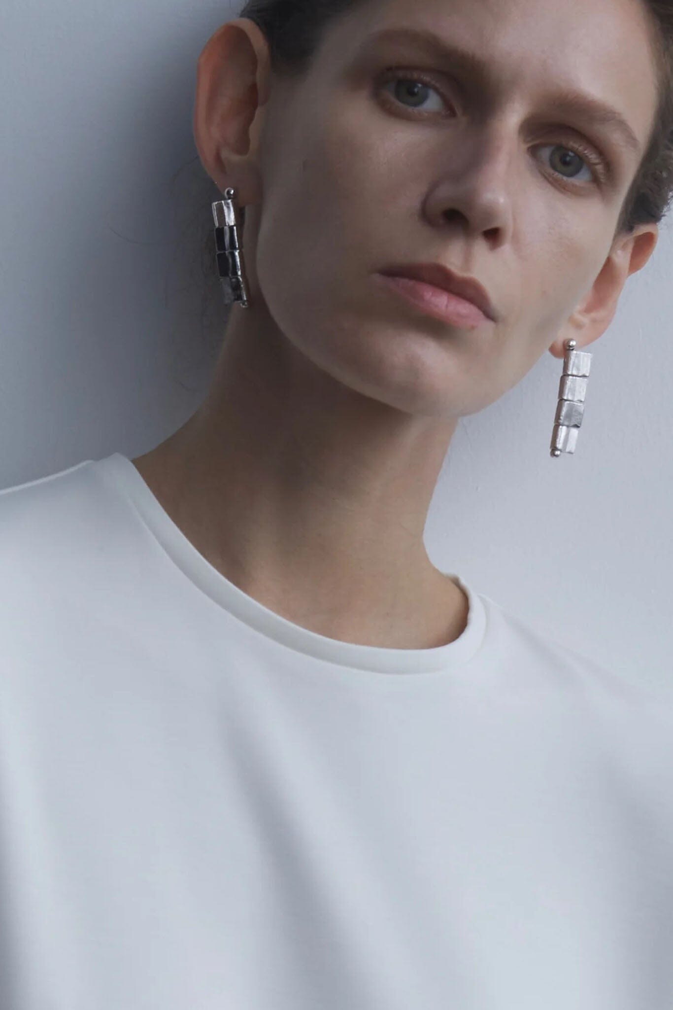 Person wearing silver earrings against a plain background