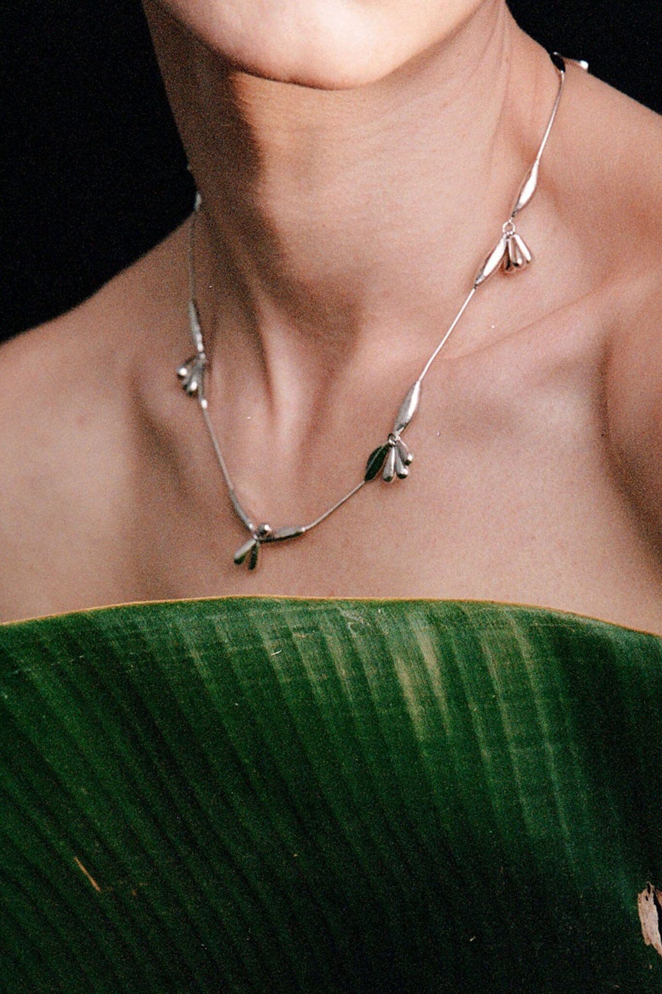 Silver necklace with floral leaf designs worn by a person against a dark background