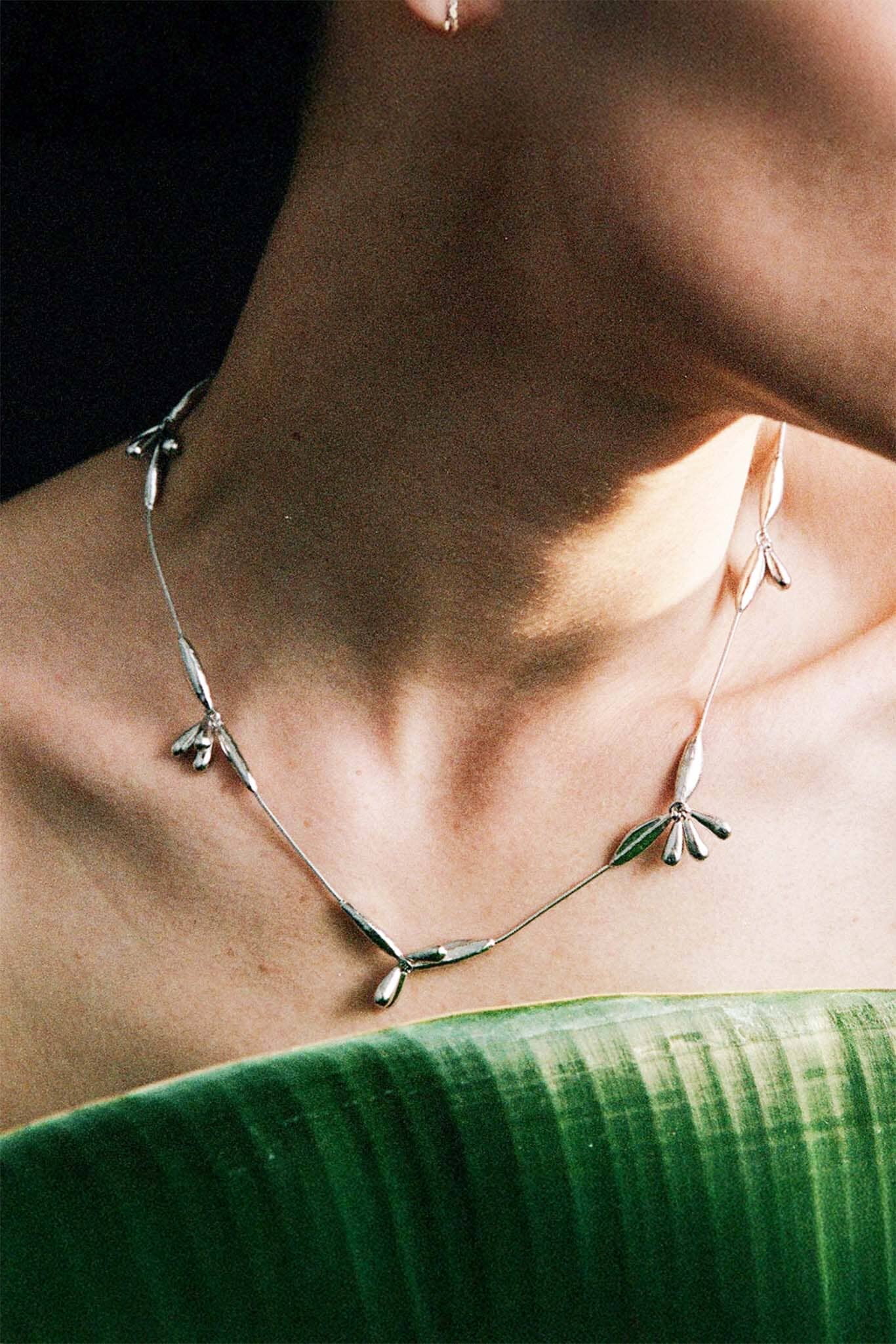 Necklace with leaf-like pendants worn by a person against a dark background