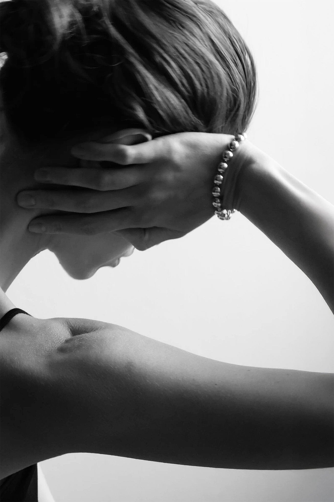 Person resting their hand on their head with a silver dome bracelet.