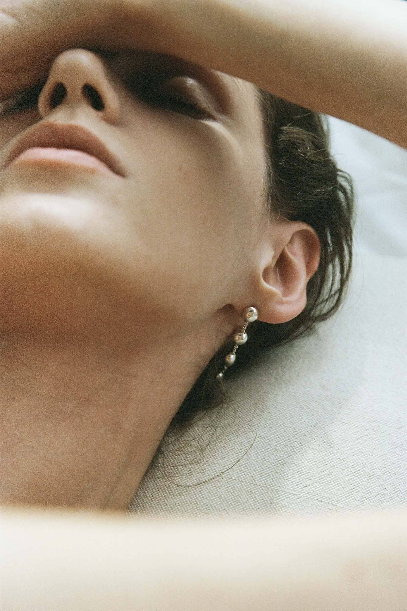 Close-up of a person wearing silver dome drop earrings on a blurred background