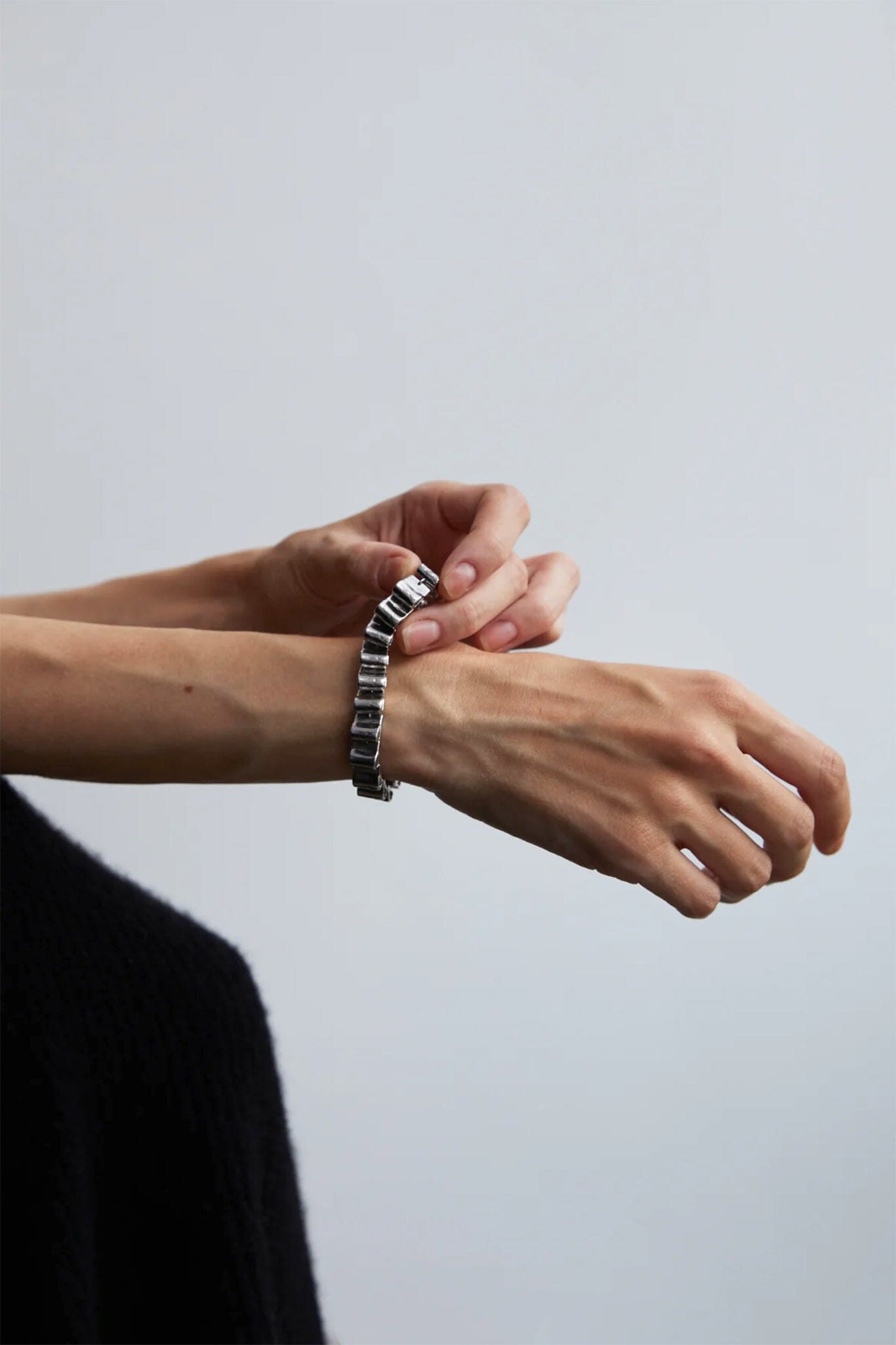 Person wearing a silver chunky bracelet on a plain background