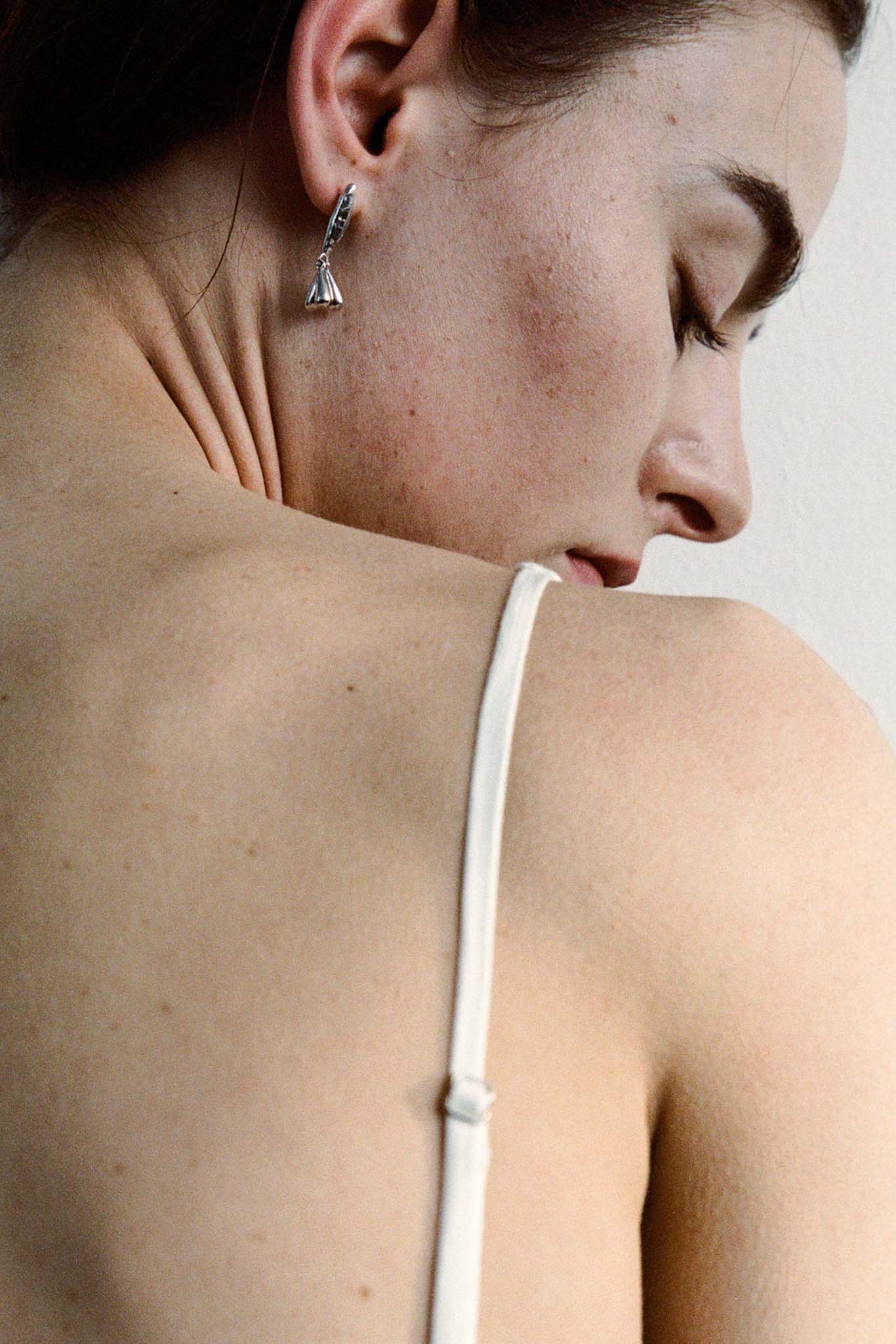 Close-up of a woman wearing silver floral drop earrings against a neutral background