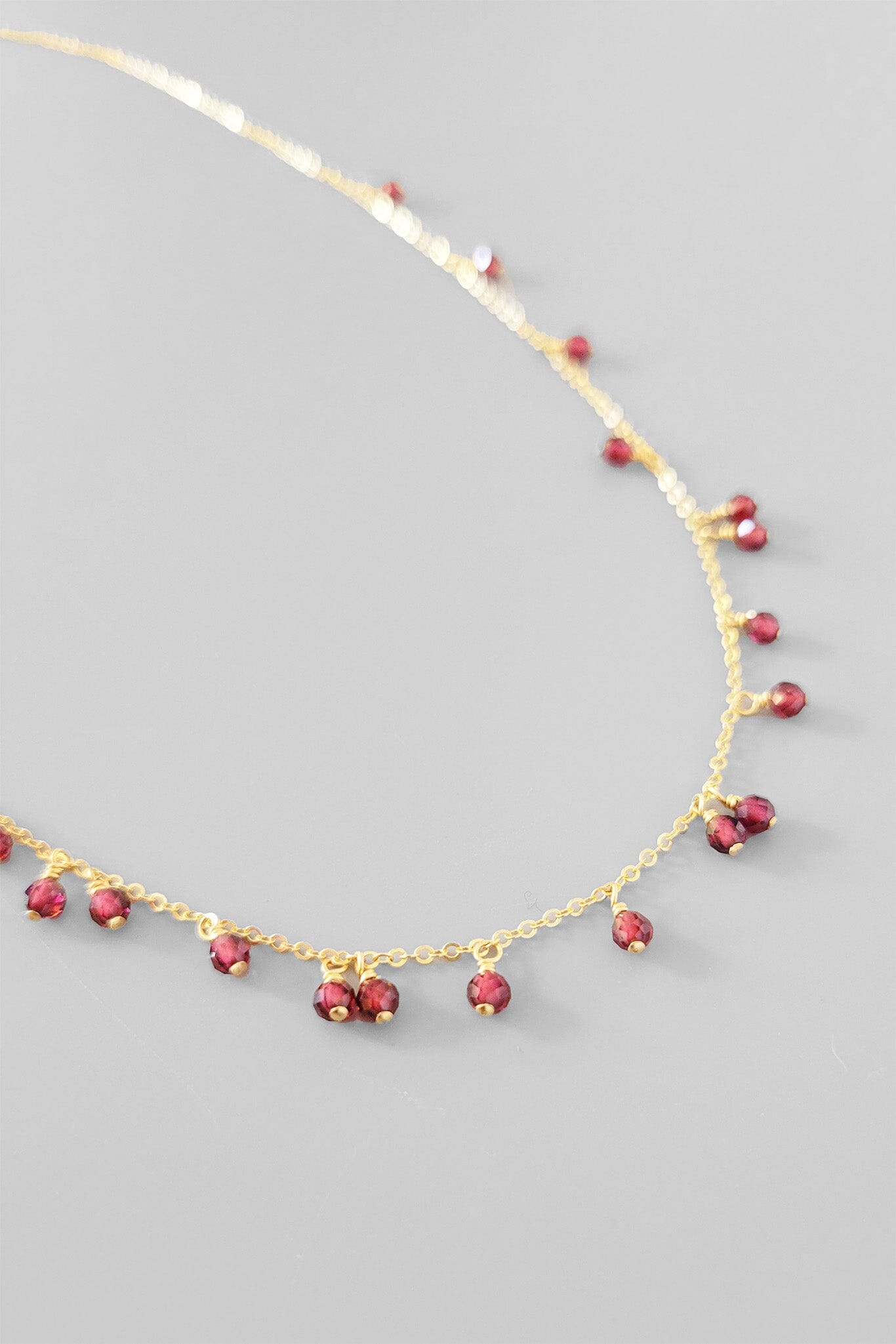 Gold necklace with red gemstones on a gray background