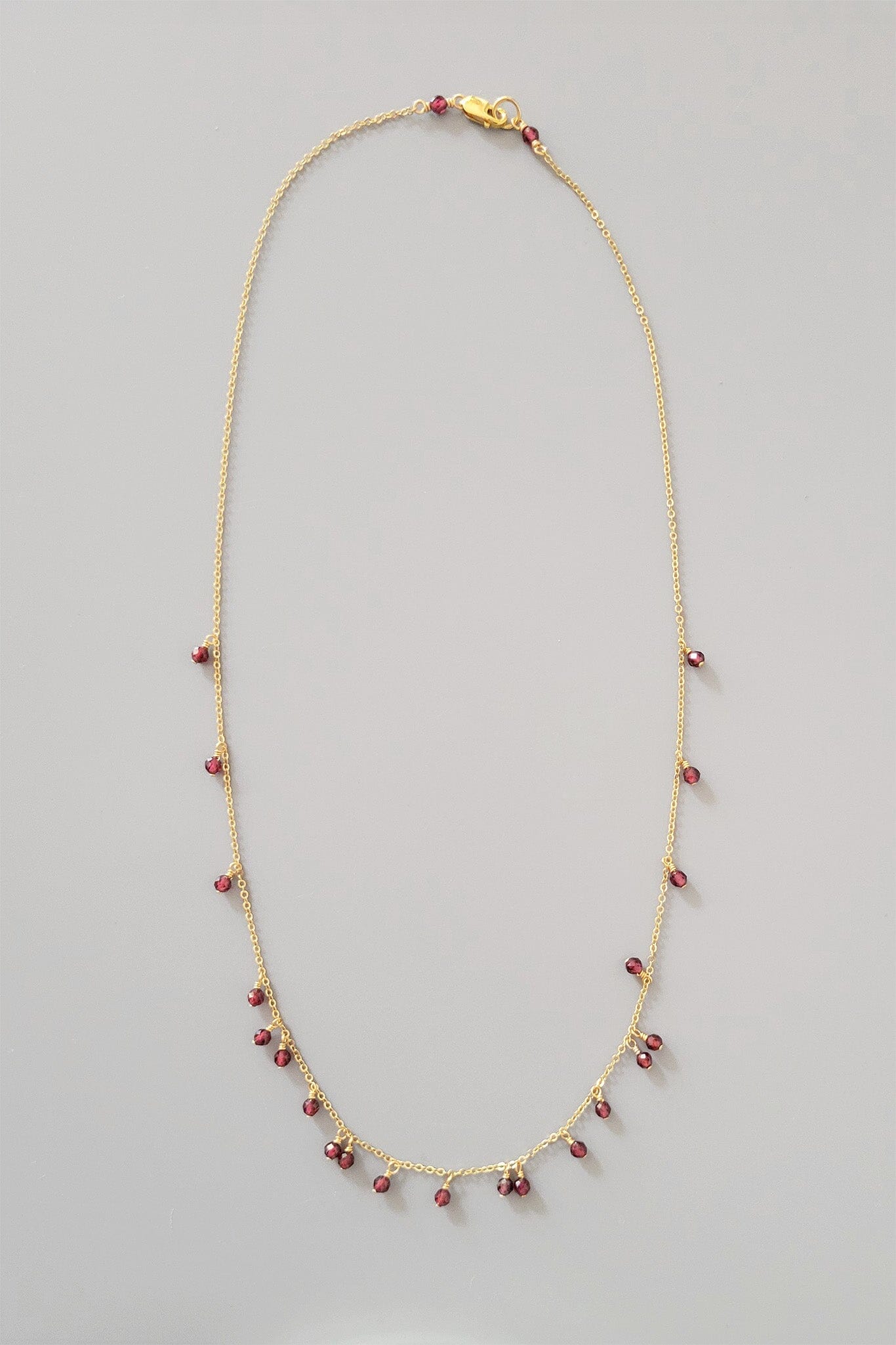 Gold necklace with garnet beads on a gray background