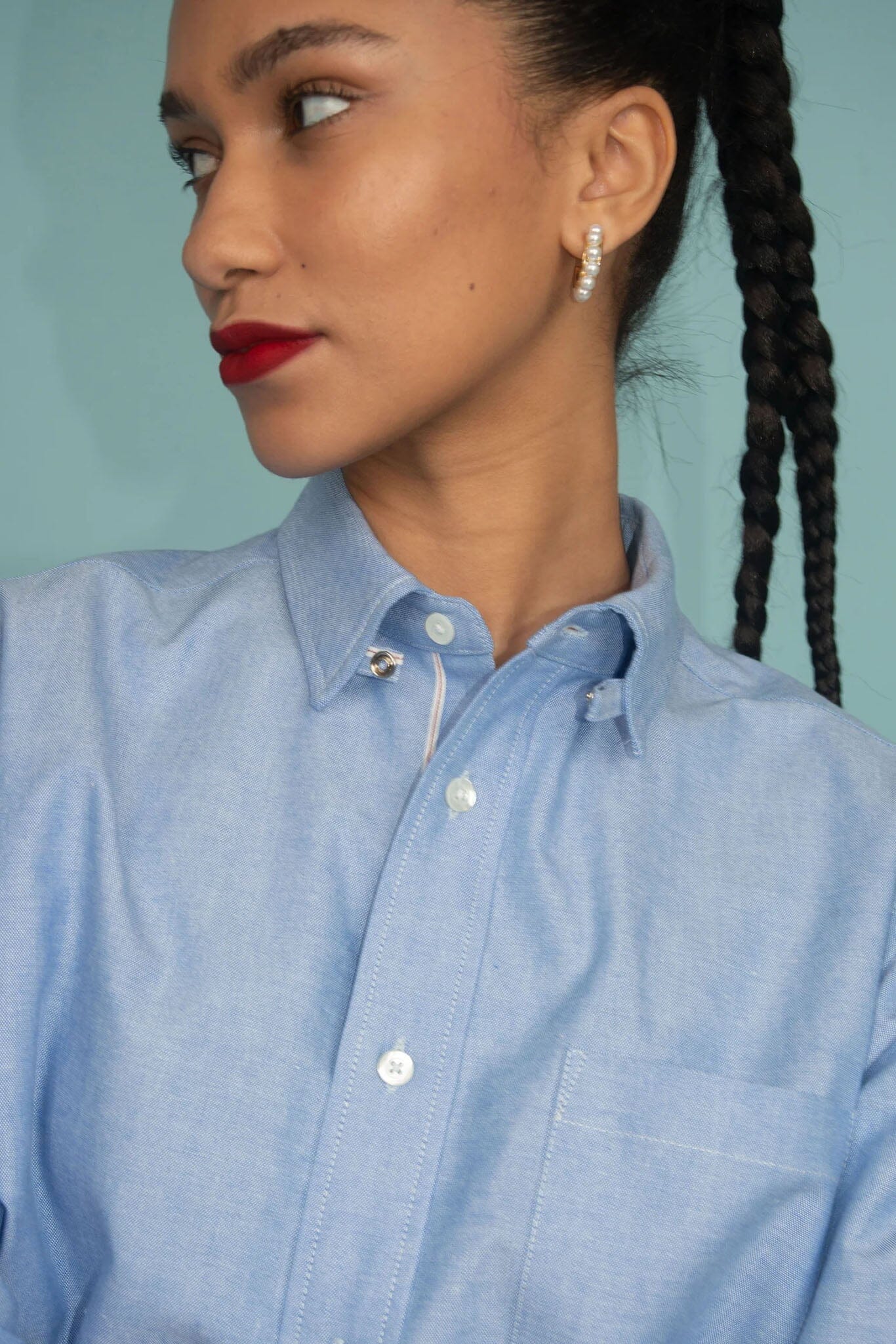 Woman wearing a light blue collared shirt with a plain background.
