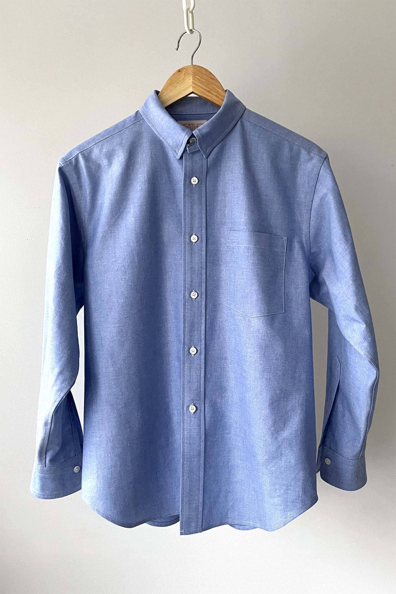 Blue long sleeved shirt on a hanger against a plain background
