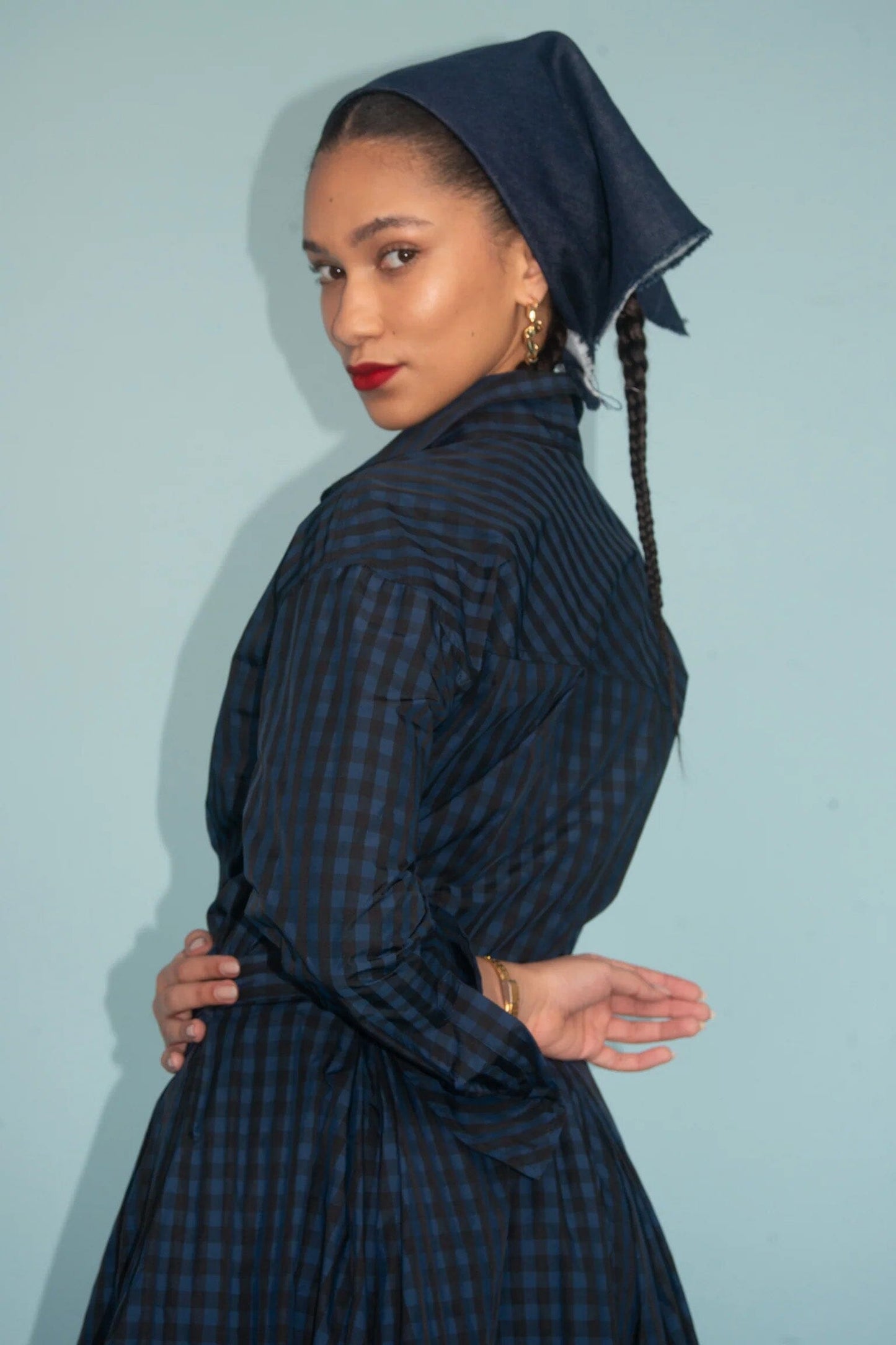 Woman wearing a dark blue checkered dress with a matching headscarf against a light blue background