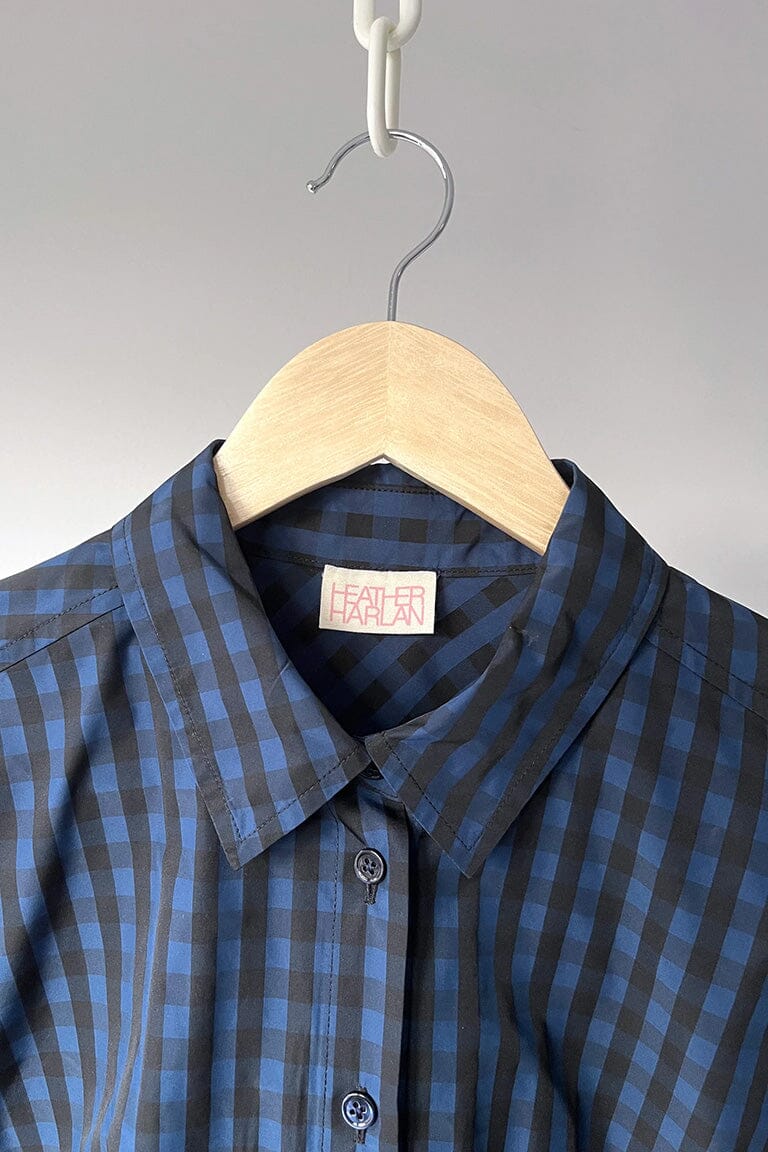 Blue and gray checkered shirt on a wooden hanger against a gray background