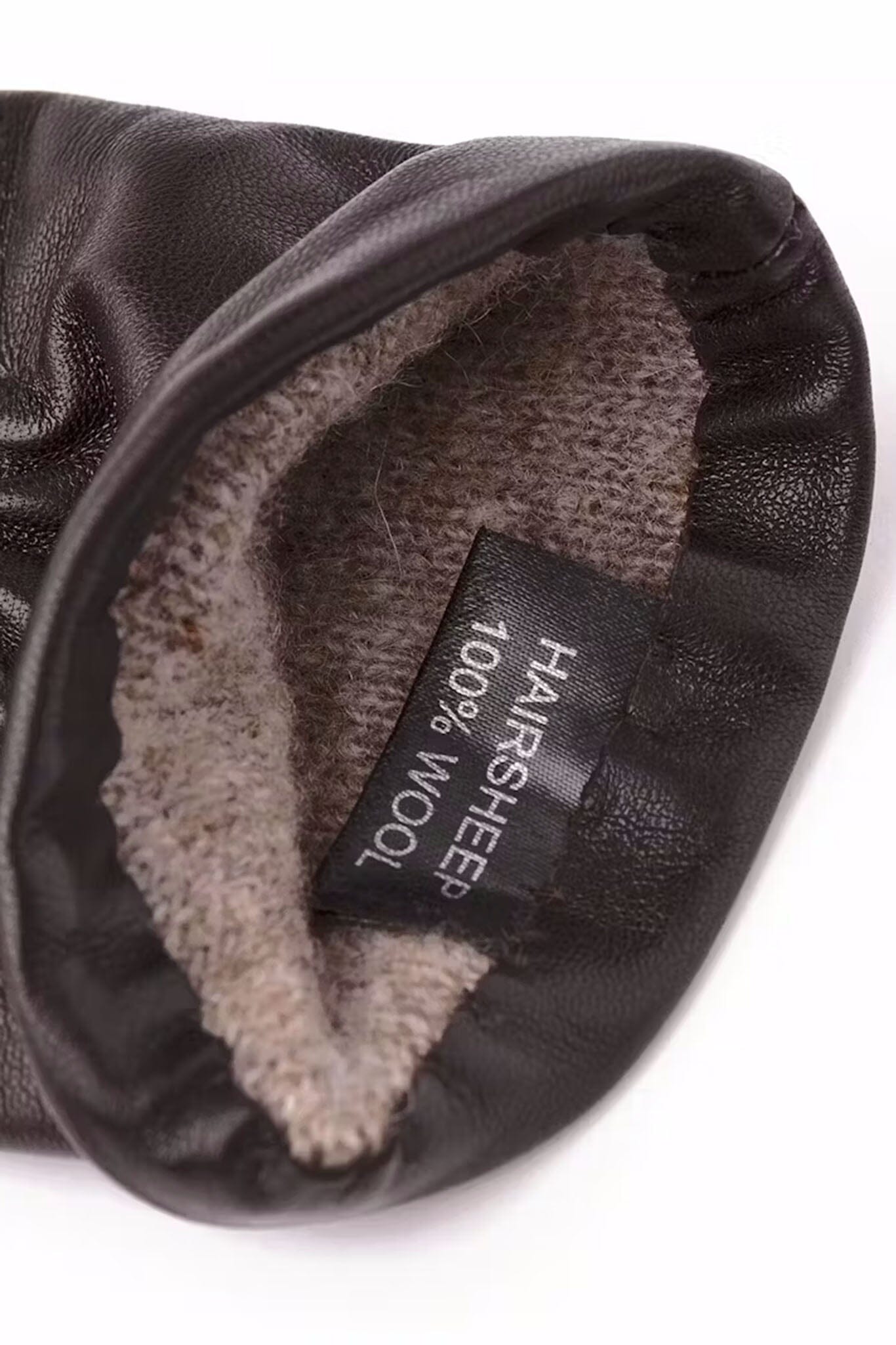 Close-up of a black leather glove with gray shearling lining and a label indicating 100% wool.