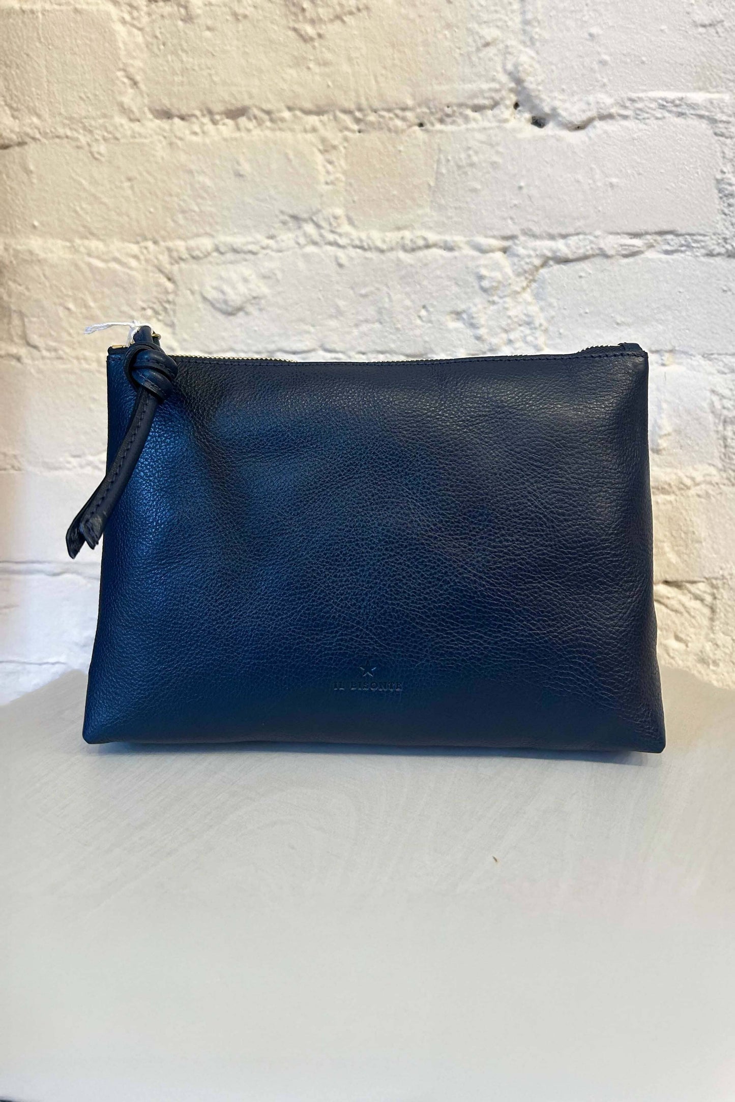 Navy leather zipper pouch on a textured white surface with a light gray background