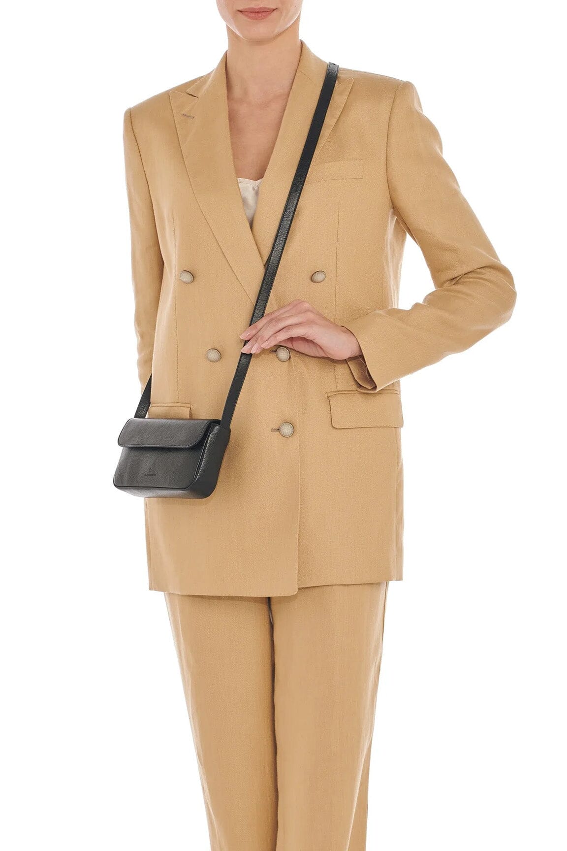 A woman in a beige pantsuit wears a black leather crossbody bag