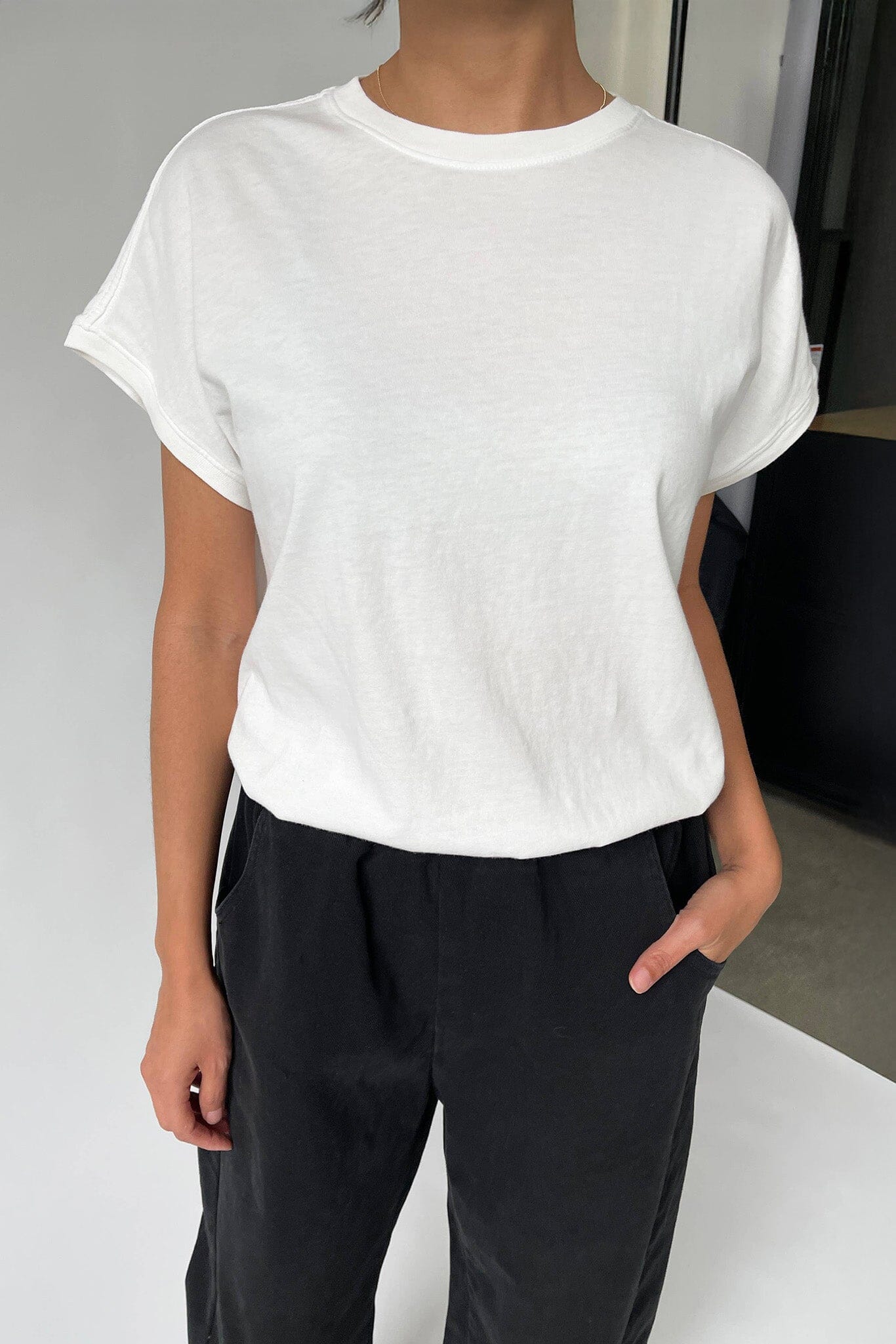 Person wearing a white t-shirt and black pants on a neutral background