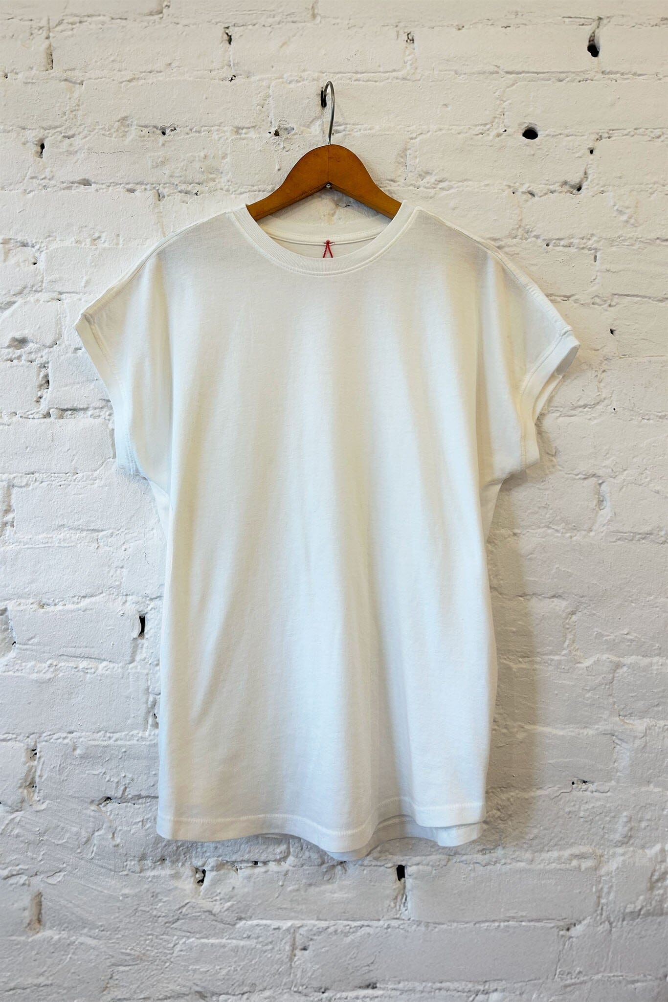 White t-shirt on a wooden hanger against a white brick wall.