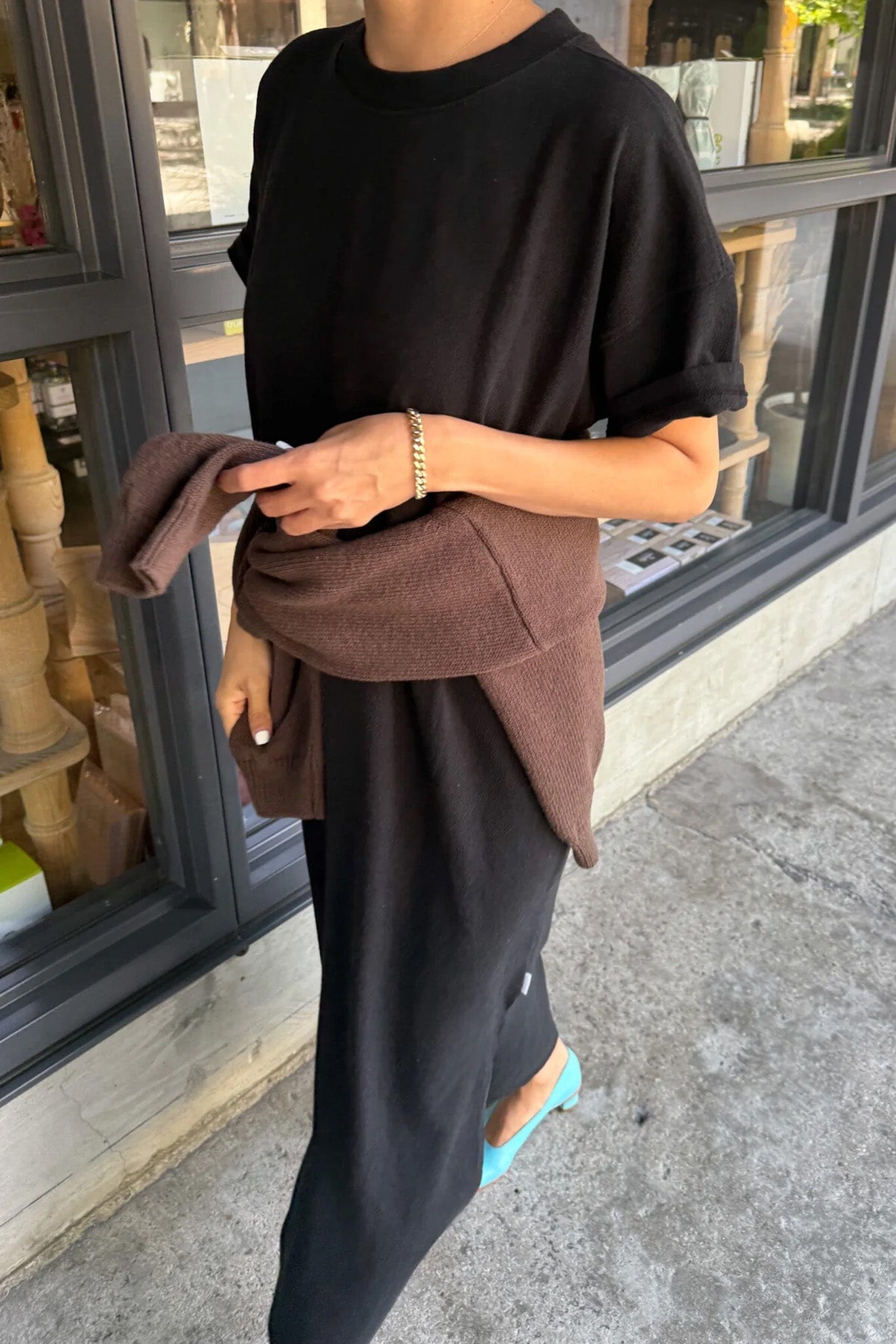 Person holding a brown bag and wearing a lightweight black cotton dress in front of a store window