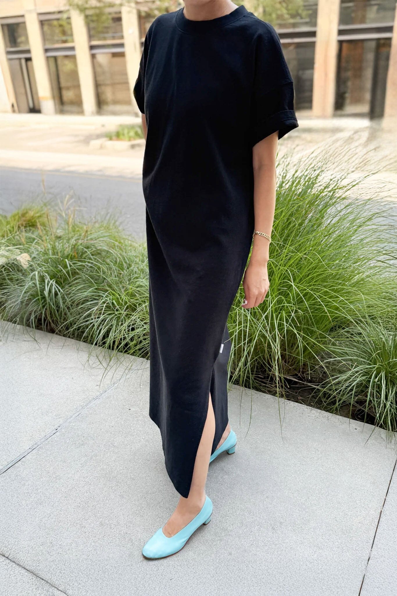 Person wearing a black dress with a slit, standing outdoors on a sidewalk.