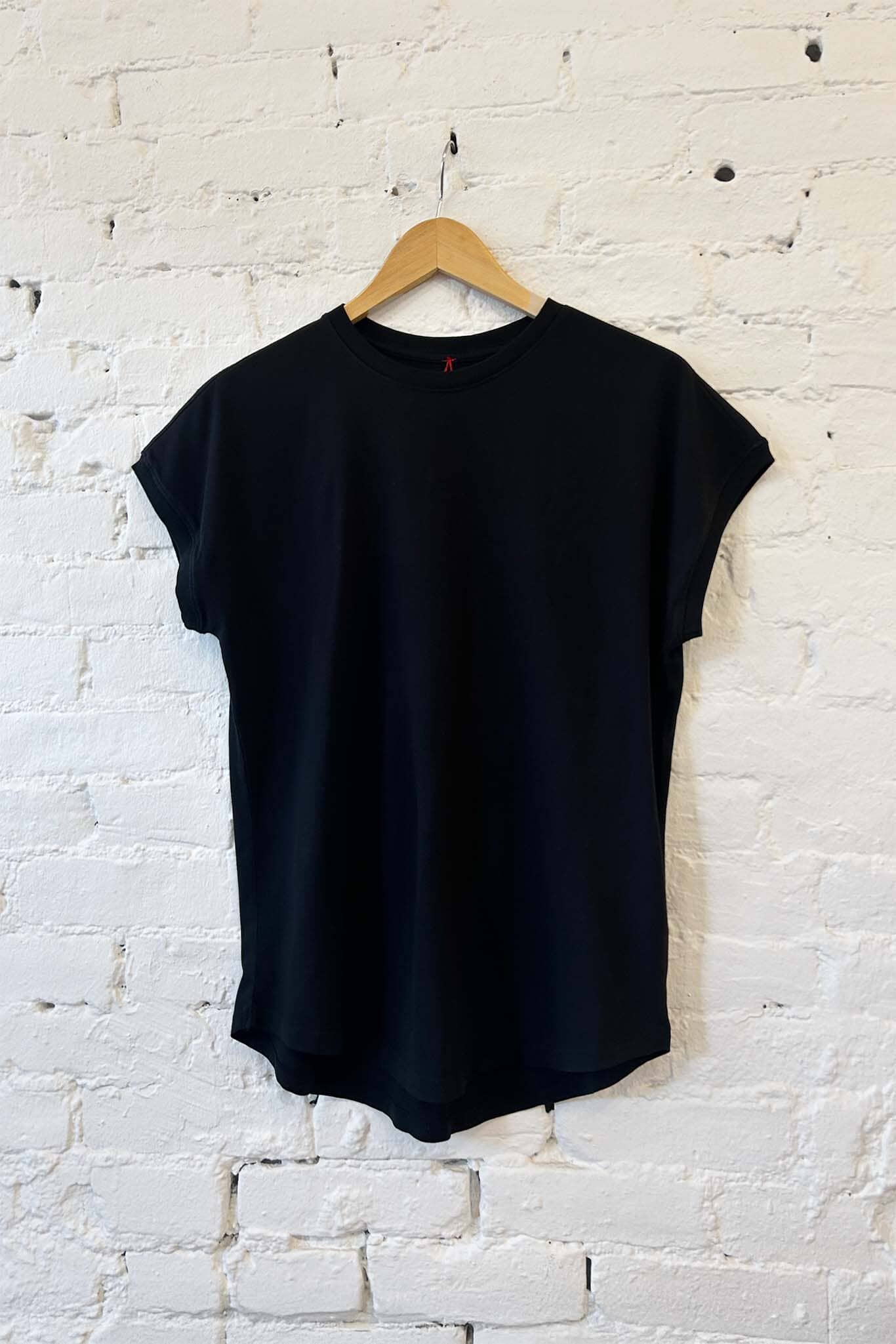 Black t-shirt on a wooden hanger against a white brick wall