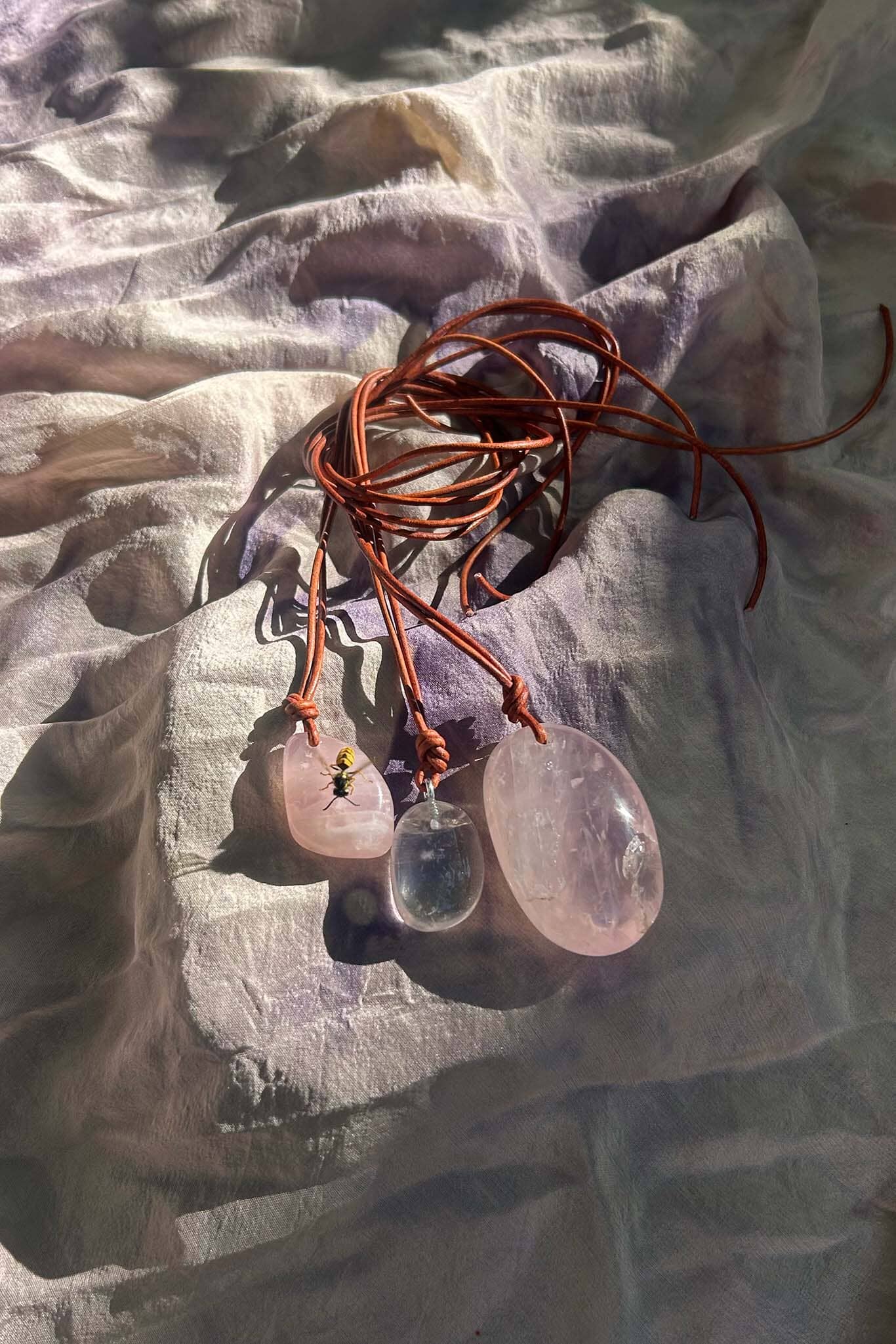 Necklaces with pink and clear stone pendants on a textured fabric background