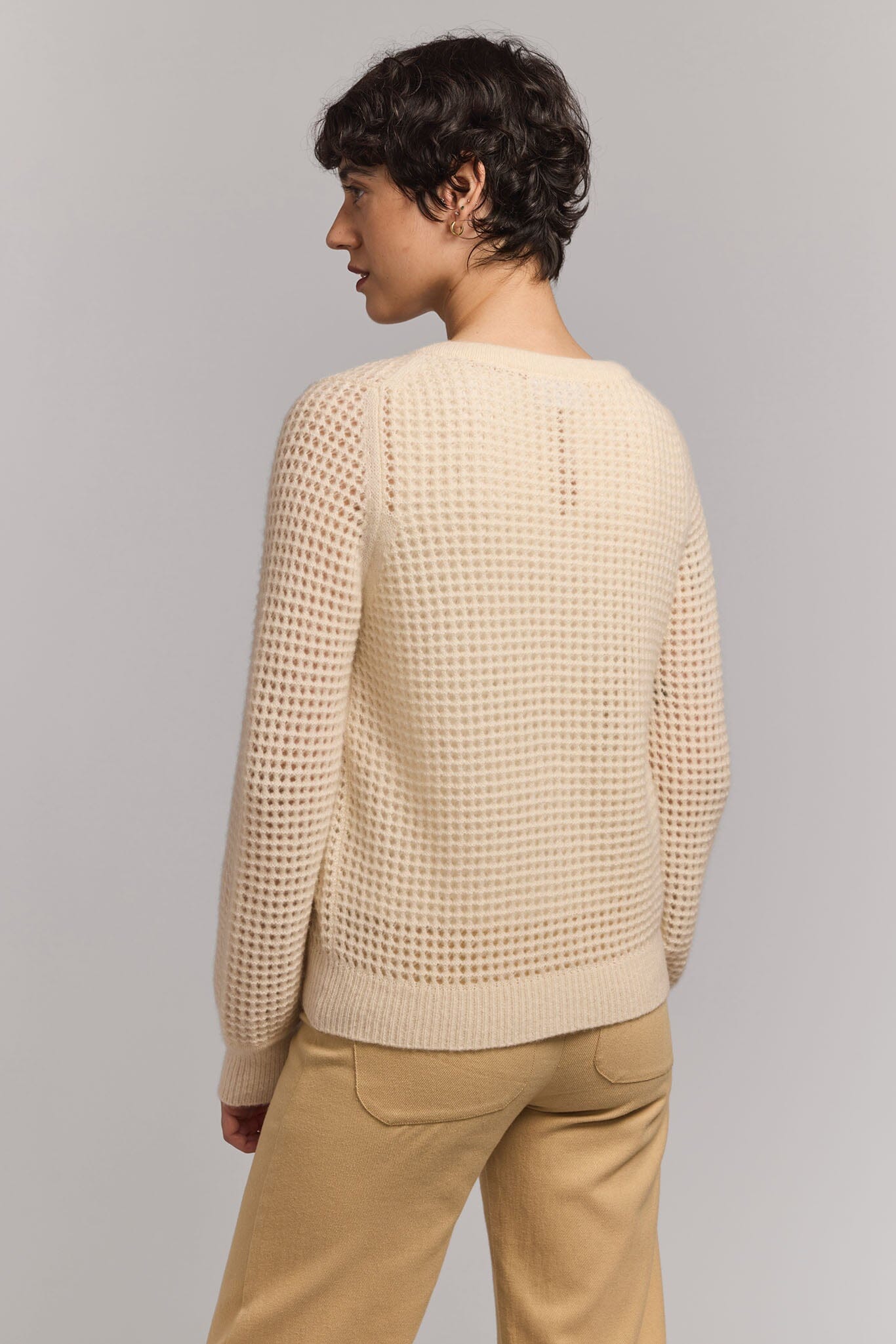 Woman wearing a beige textured sweater and beige pants on a plain background