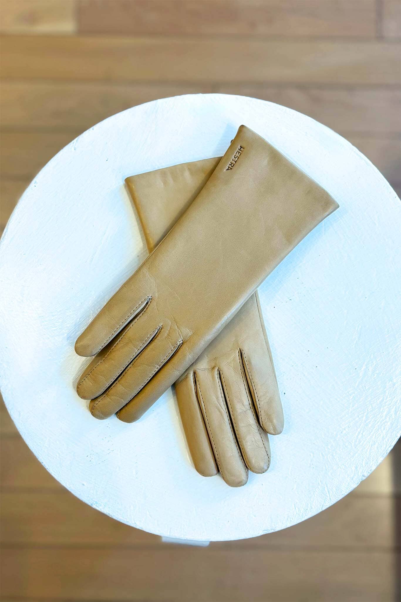 Pair of beige gloves on a white surface with a wooden background