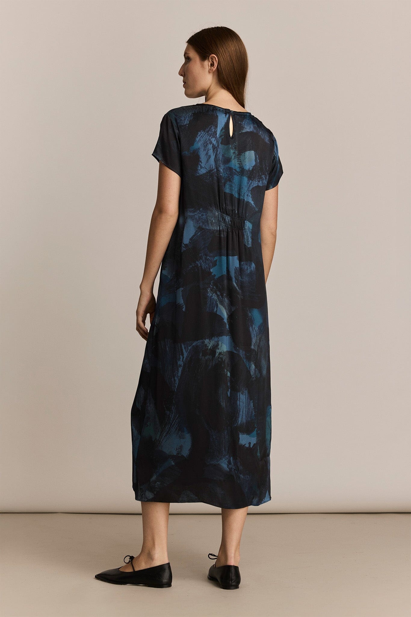 Woman wearing a blue patterned silk short sleeve dress against a beige background