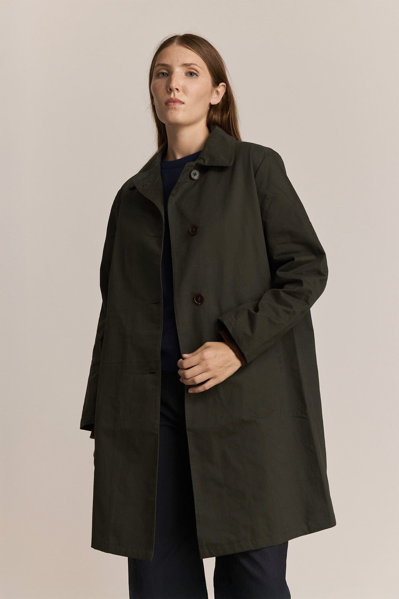 Woman wearing a dark green trench coat against a plain background