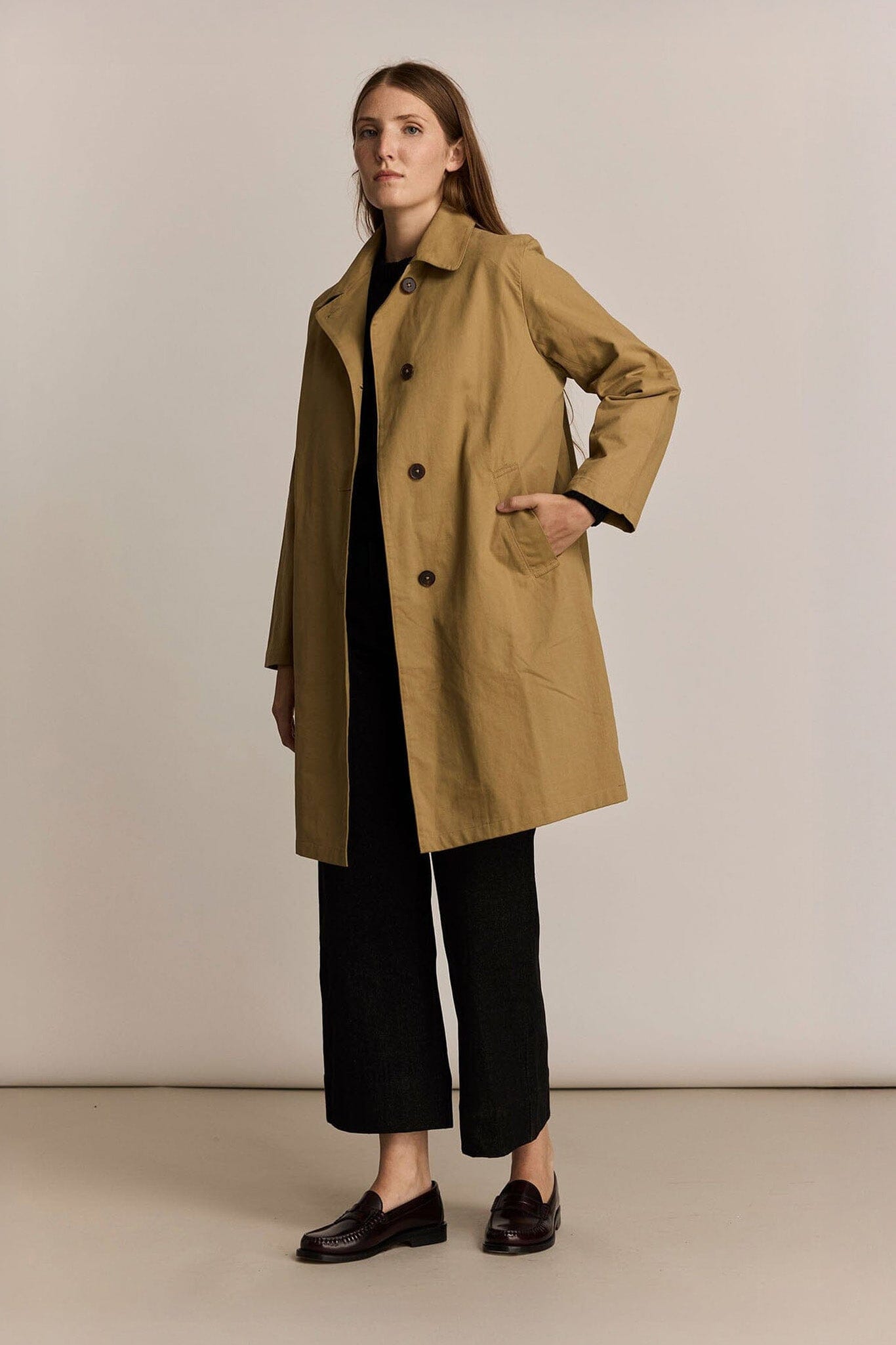 Woman wearing a beige trench coat with pockets against a plain background
