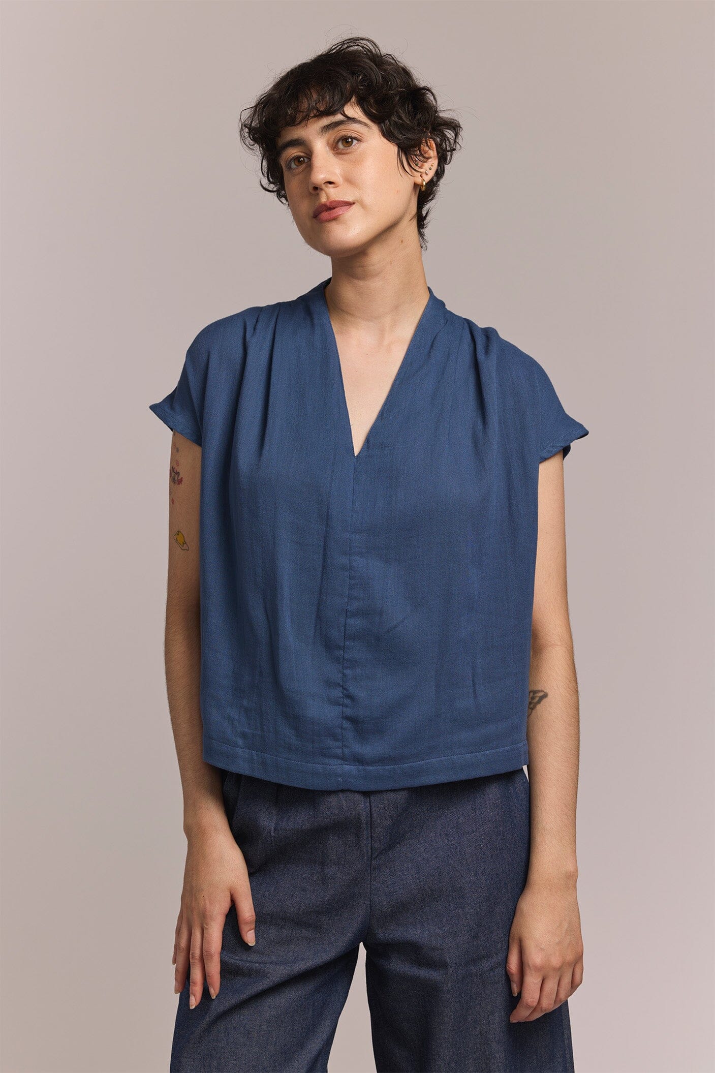 Person wearing a blue top and dark pants against a plain background