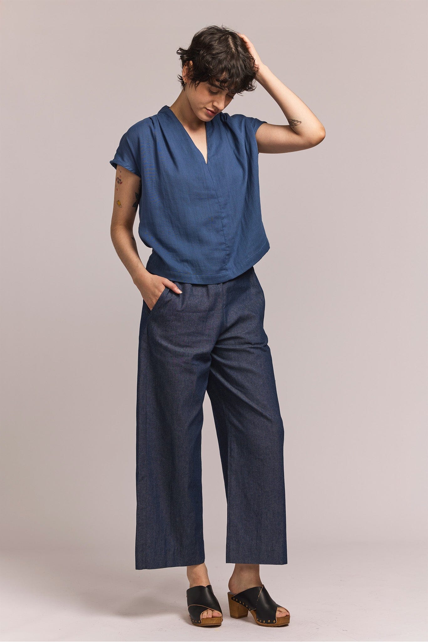 Person wearing a blue v-neck blouse with denim pants against a plain background