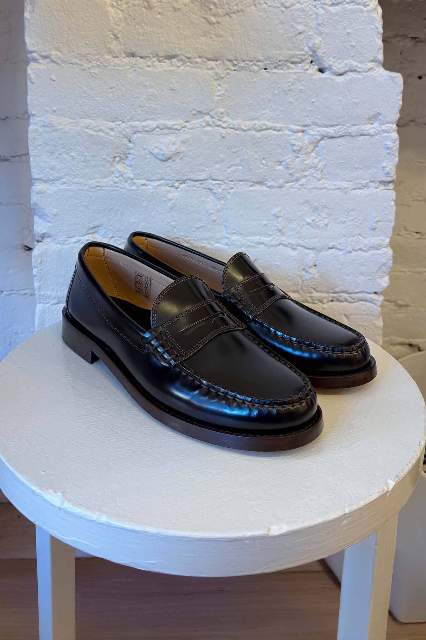 Black loafers on a white stool against a white brick wall