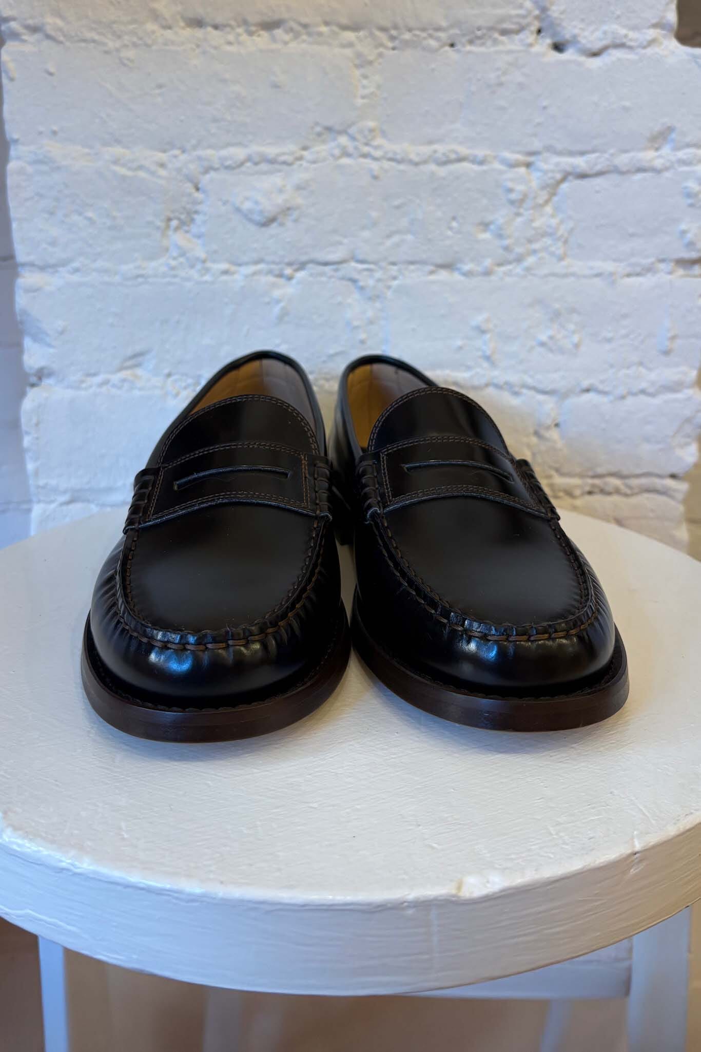 Pair of black loafers on a white stool with a white brick wall background