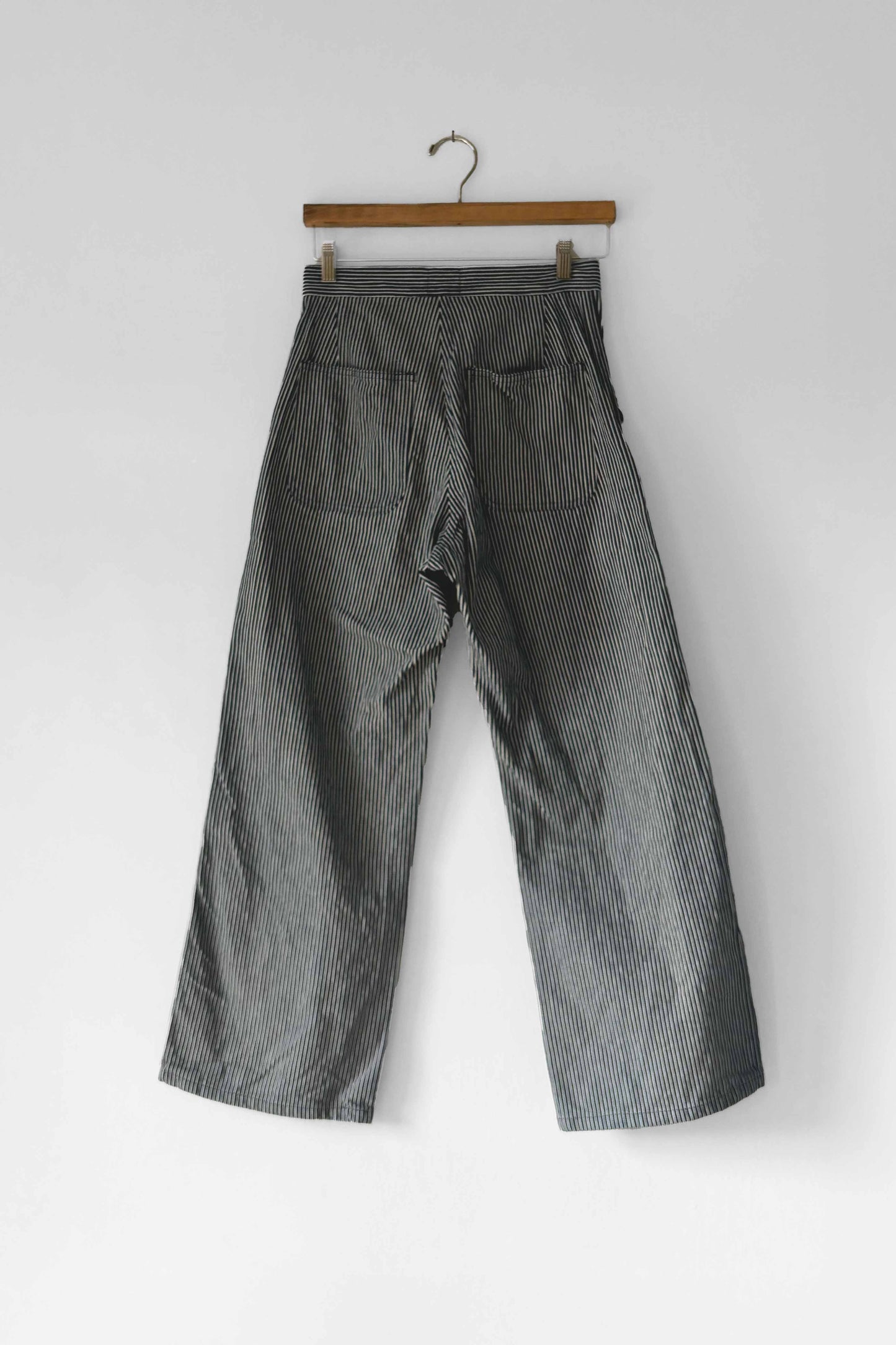 The back view of high-rise, wide-leg grey sailor pants with button fly and striped pattern, displayed on a hanger against a white background.