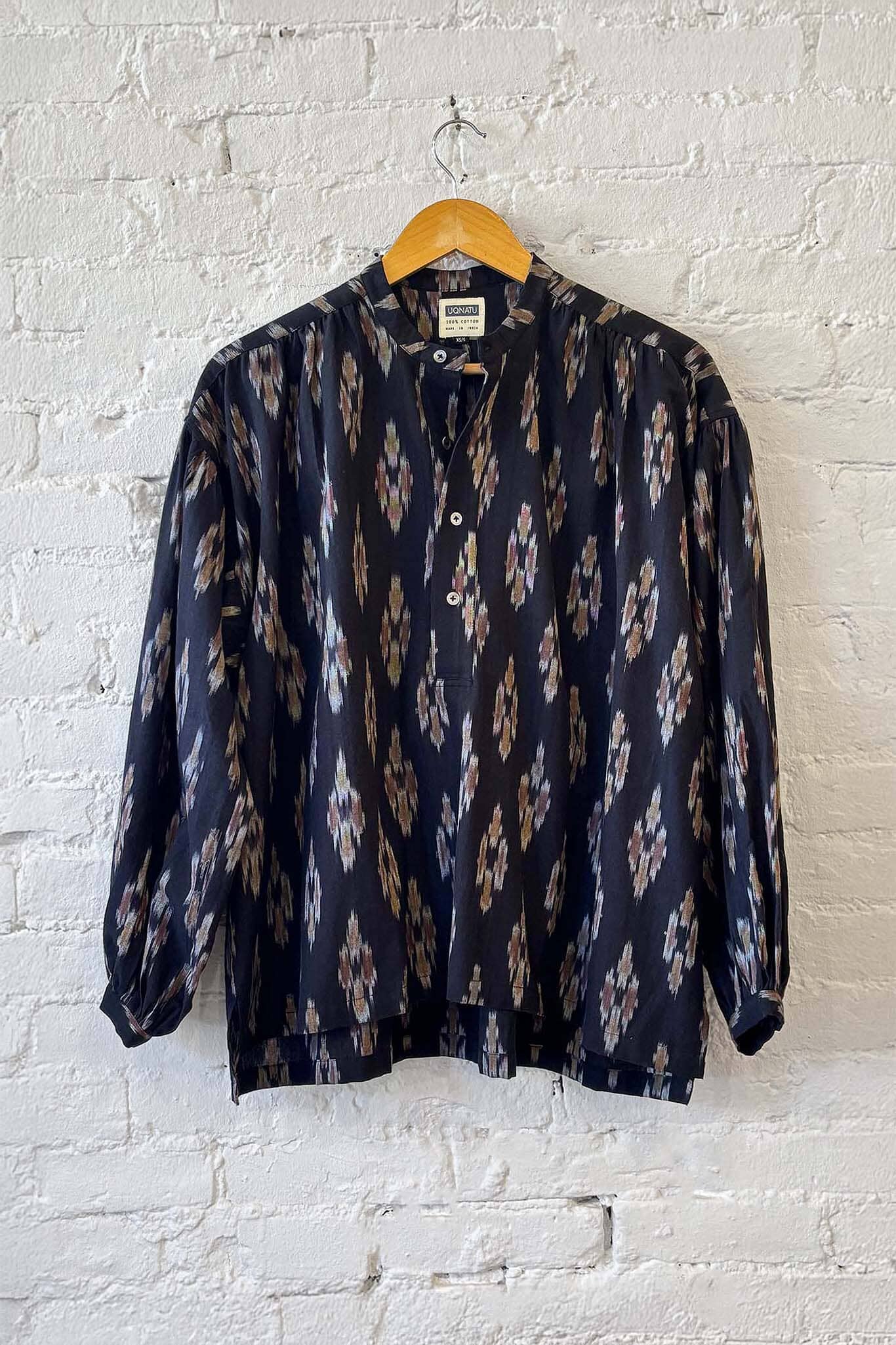 Patterned long sleeve blouse on a hanger against a white brick wall