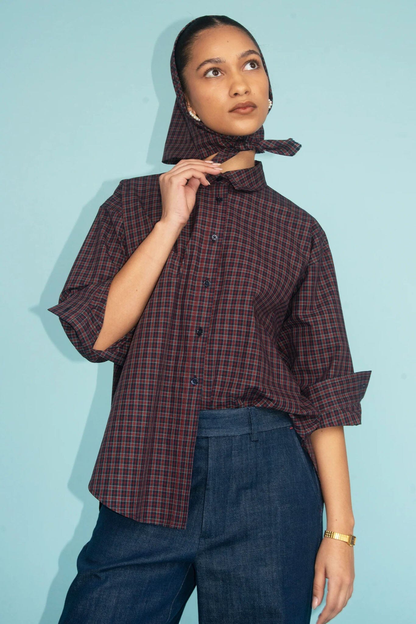 Woman wearing a plaid shirt and scarf against a light blue background
