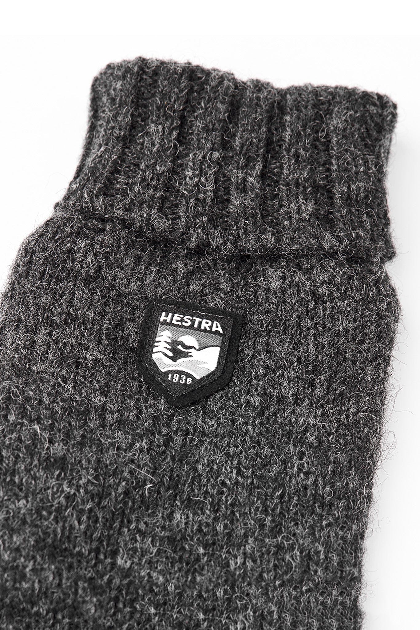A close up of charcoal gray Hestra Basic Wool Gloves laid flat against a white background.