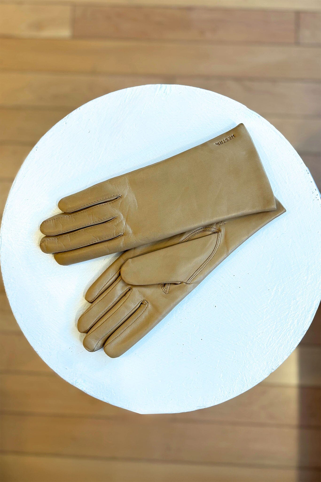 Pair of tan leather gloves on a white circular platform with a wooden background