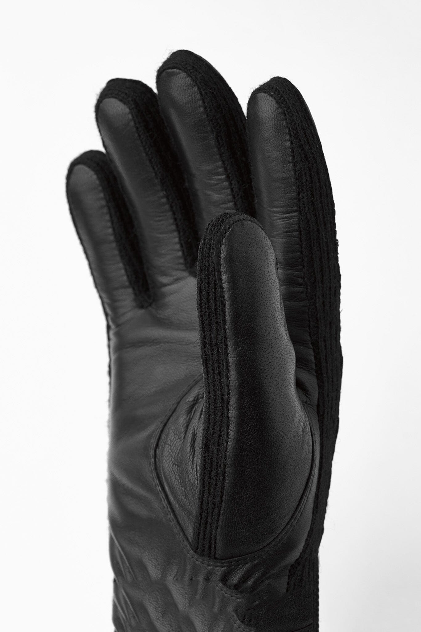 A close up of a black glove with elastic wrist cuffs and a knitted wool lining, made of leather and wool.