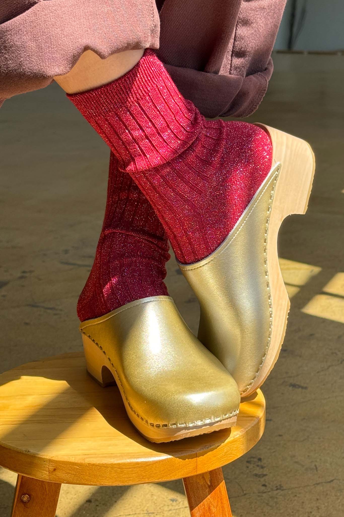 A person wearing red glitter socks with gold clogs