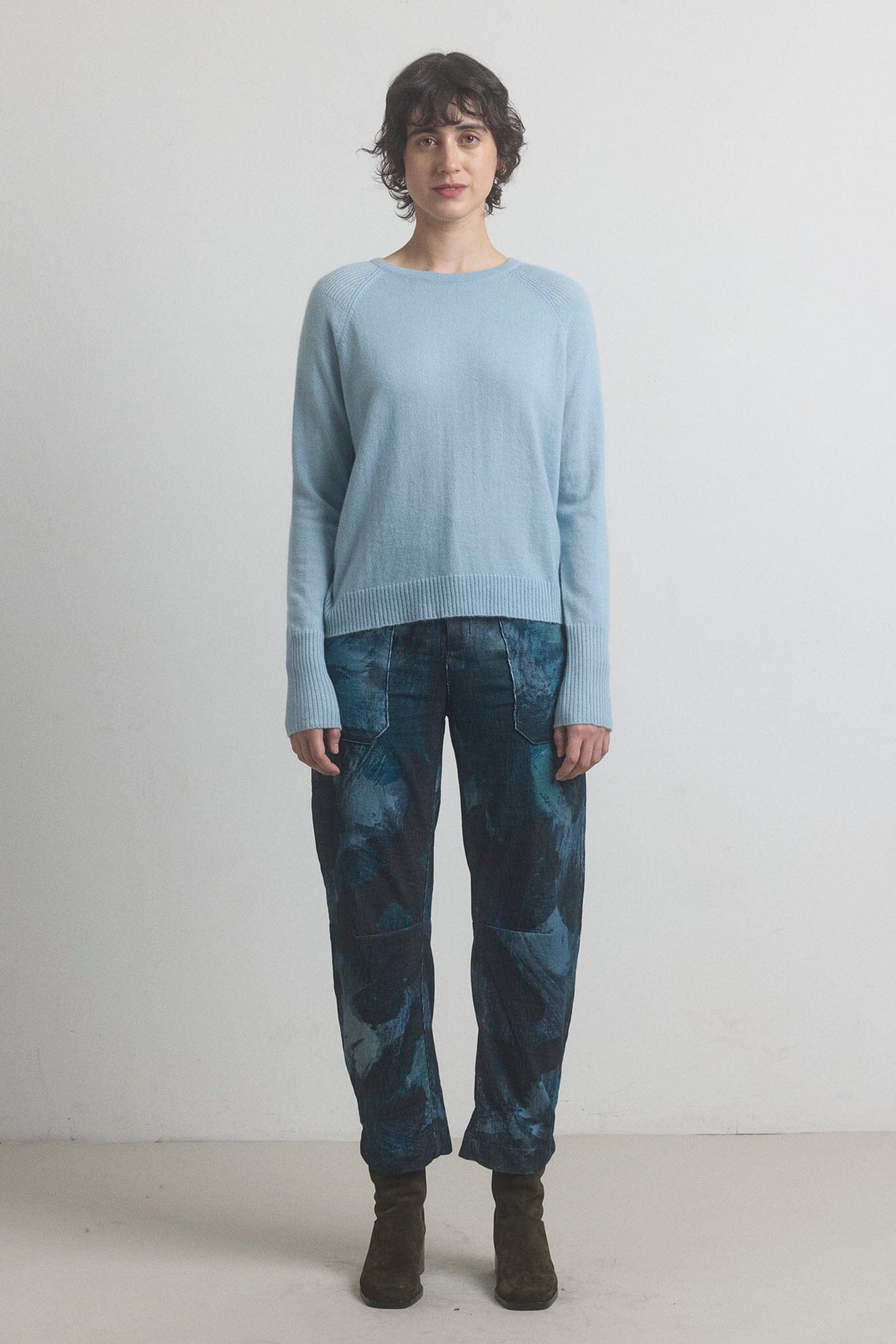 Person wearing a light blue sweater and dark patterned navy pants against a white background