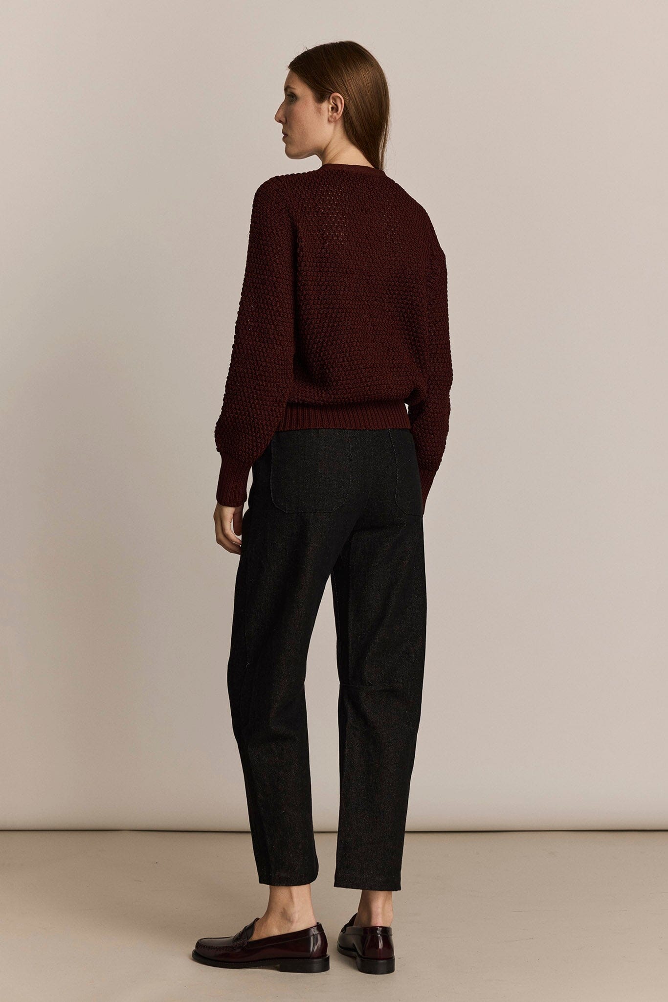Person wearing a burgundy sweater and black pants against a beige background