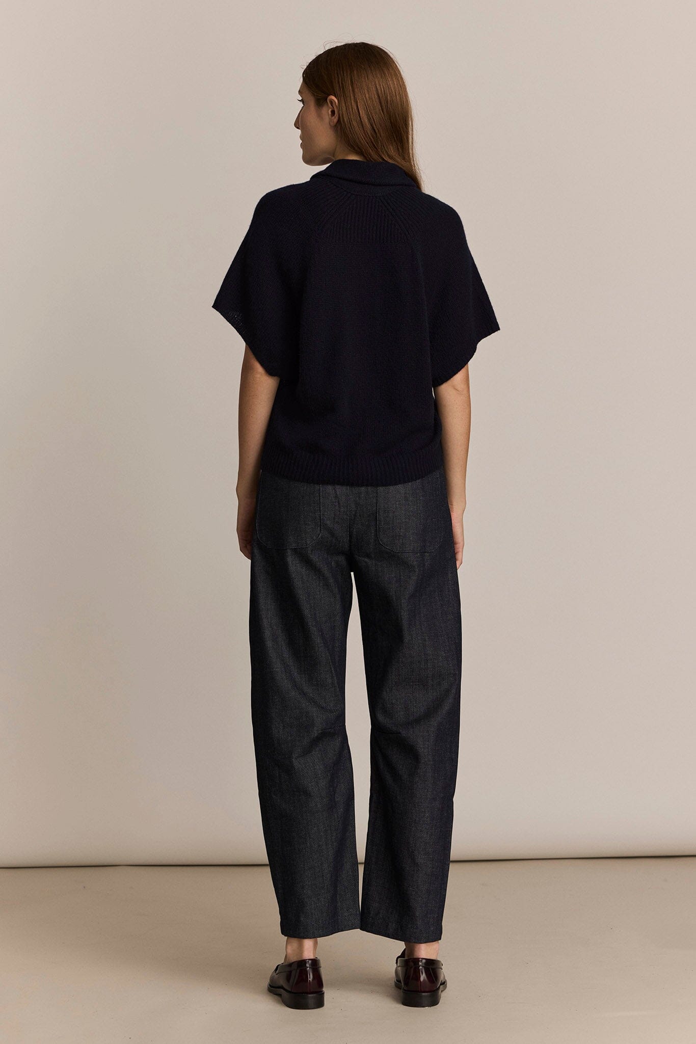 Person wearing a black sweater and dark pants against a beige background