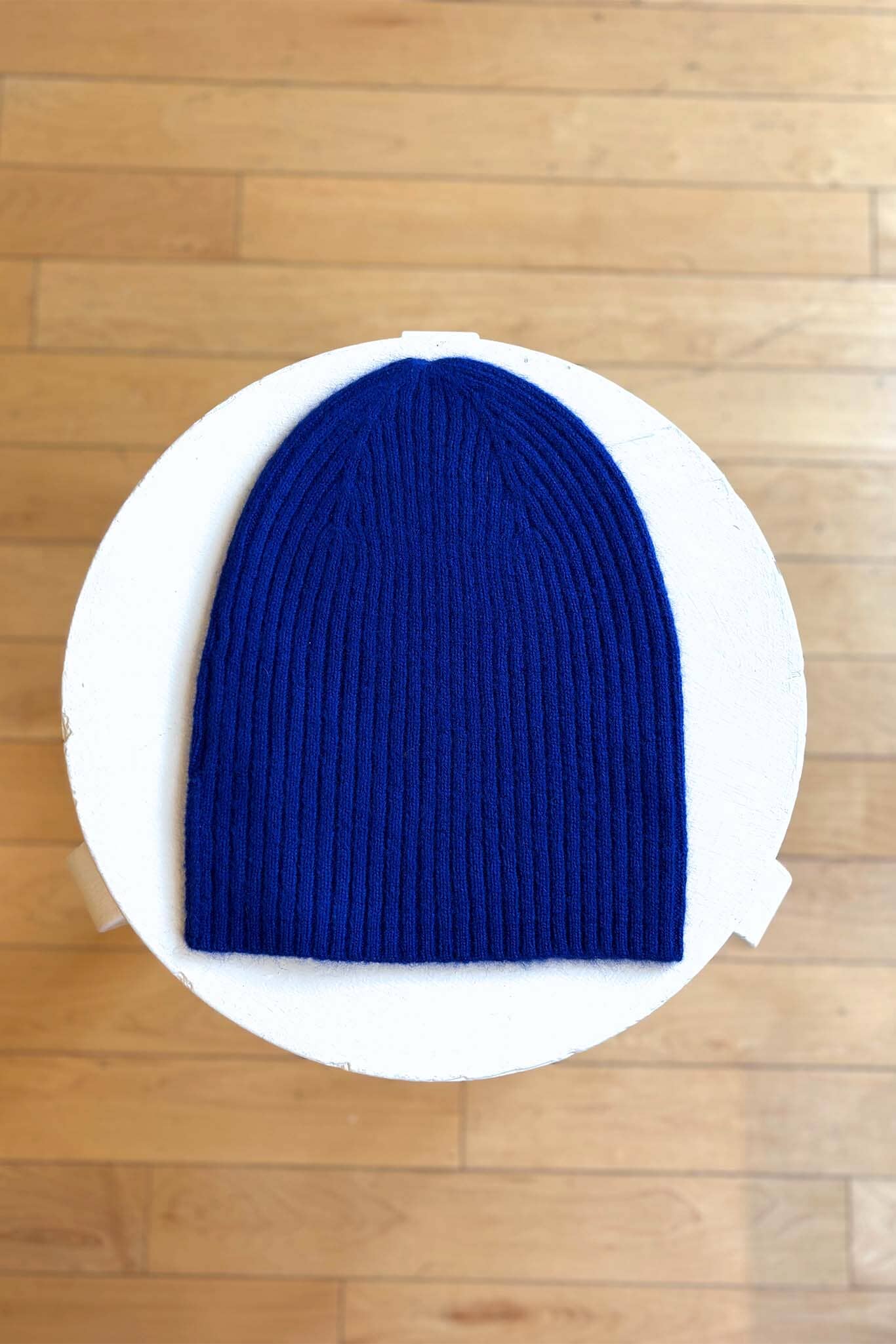 Cobalt blue knit beanie on a white circular platform with a wooden floor background