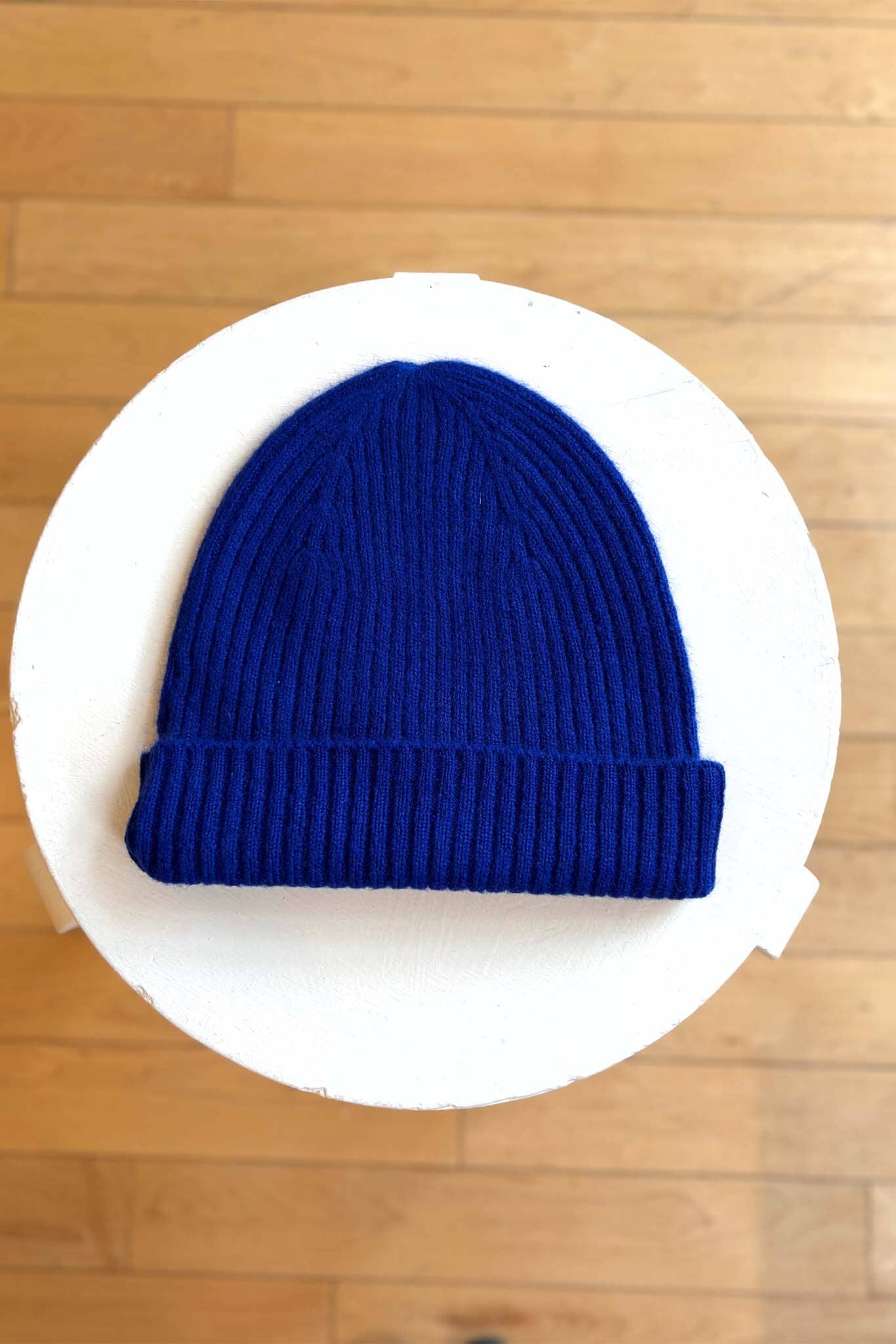 Blue knit beanie on a white circular platform with a wooden floor background